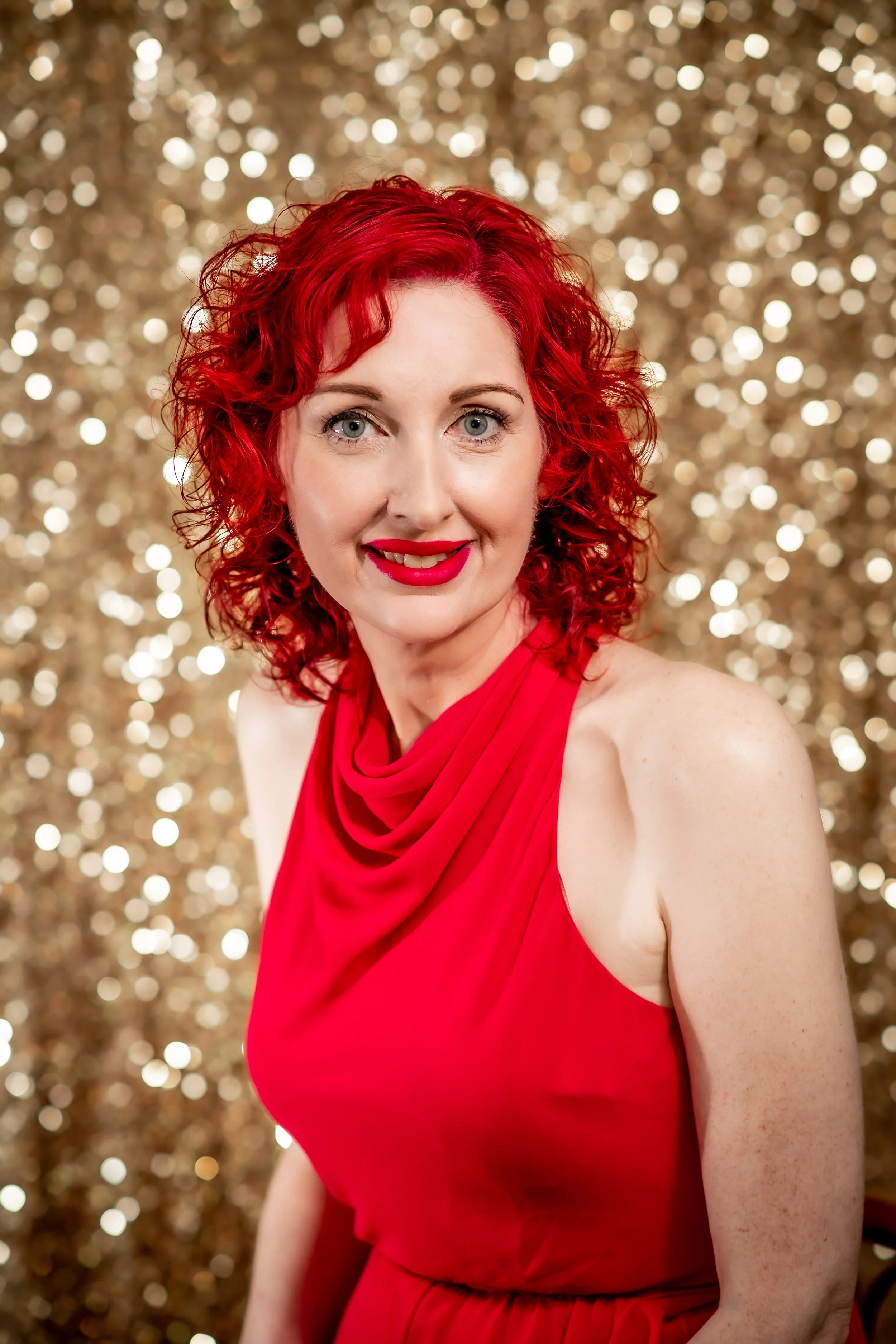 Michi Medley, LMSW, A-CAS of Ala Therapy Collective; a woman with curly red hair in a red dress against a gold glitter background. Specializing in ADHD, autism, and chronic pain therapy for youth in Oklahoma.