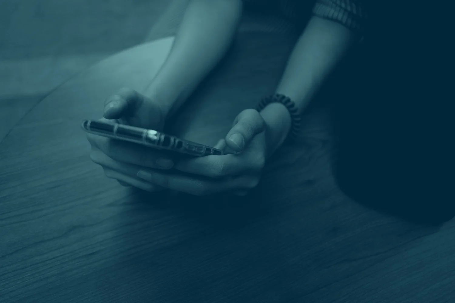 Two hands resting around a phone on a wooden table, no message being sent