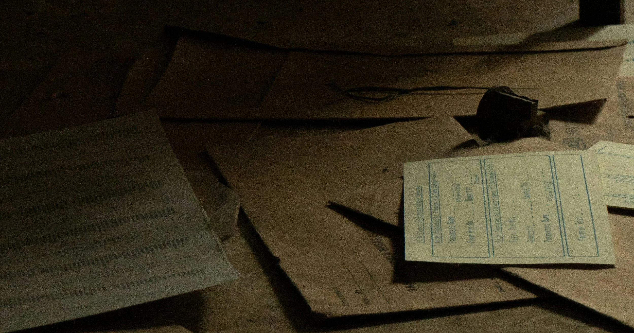 Abandoned paperwork scattered across a wooden table in a dark room, forms left unfilled
