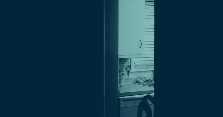 A lit kitchen seen through a narrow gap in a doorway, the rest of the room dark