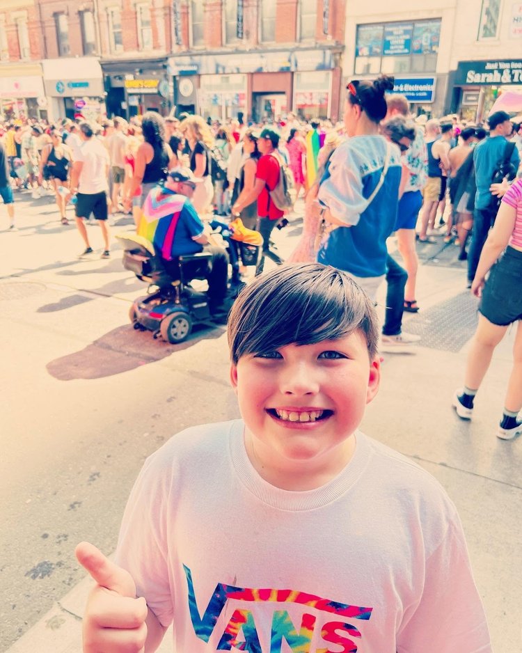 Child smiling and giving a thumbs up at a Pride street festival