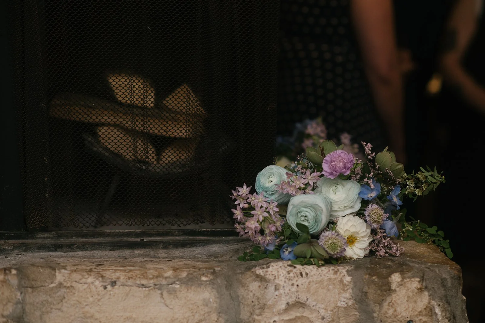 A bouquet of pastel-colored flowers resting on a stone surface next to a fireplace with logs inside at Auberge du Pommier during a wedding reception.