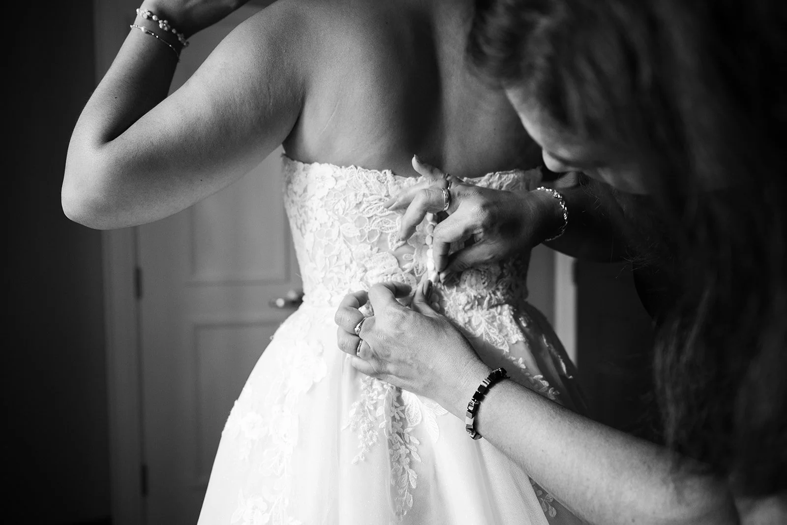 black and white photo of a mother buttoning up her daughters wedding dress.