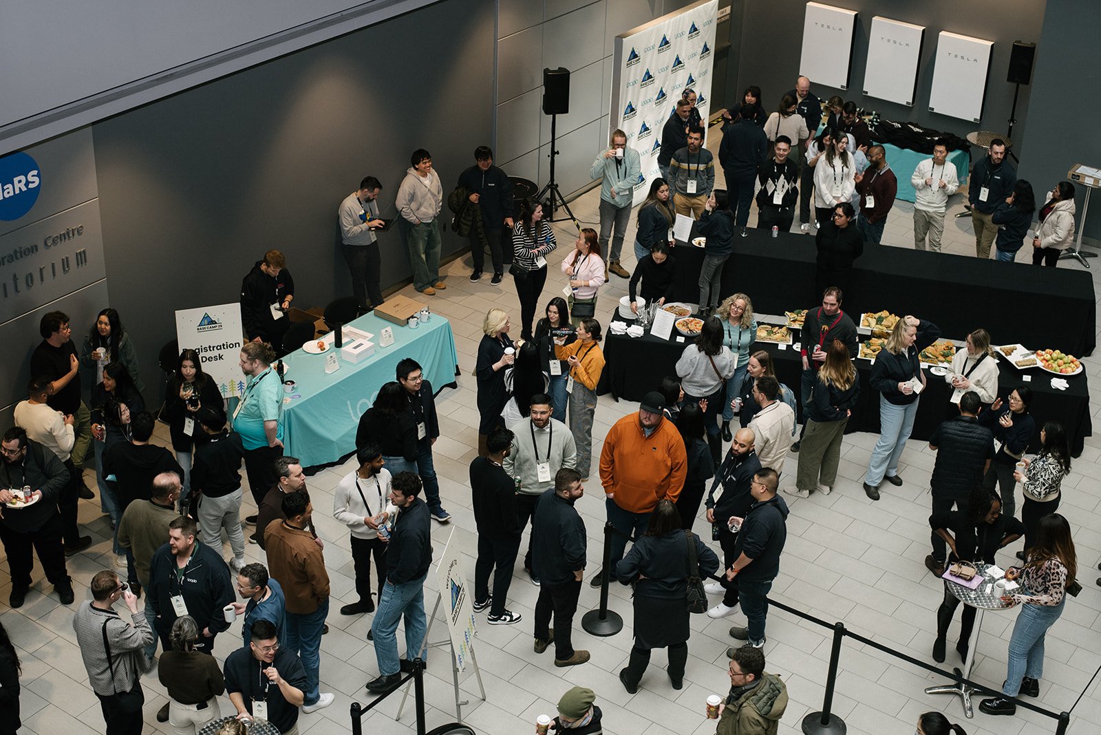 A Crowd of young professionals networking at a conference in the MaRS Discovery District in Toronto with catering tables, registration desk.