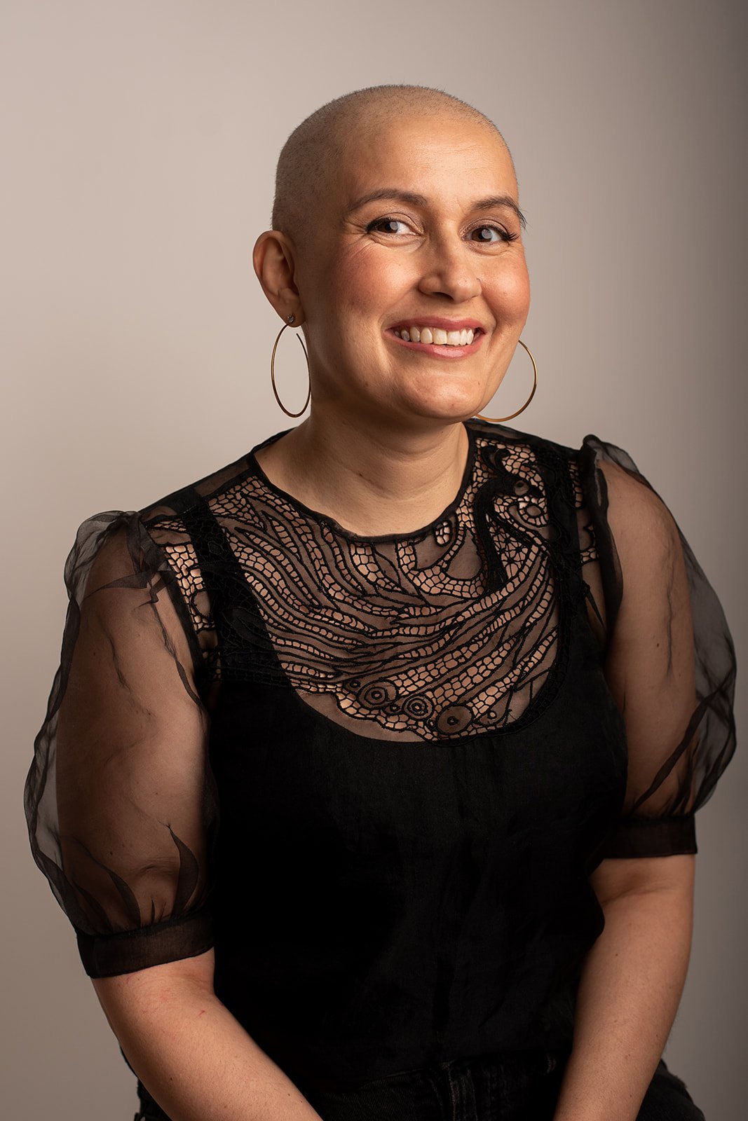 Smiling woman, wearing large hoop earrings and a black lace blouse.