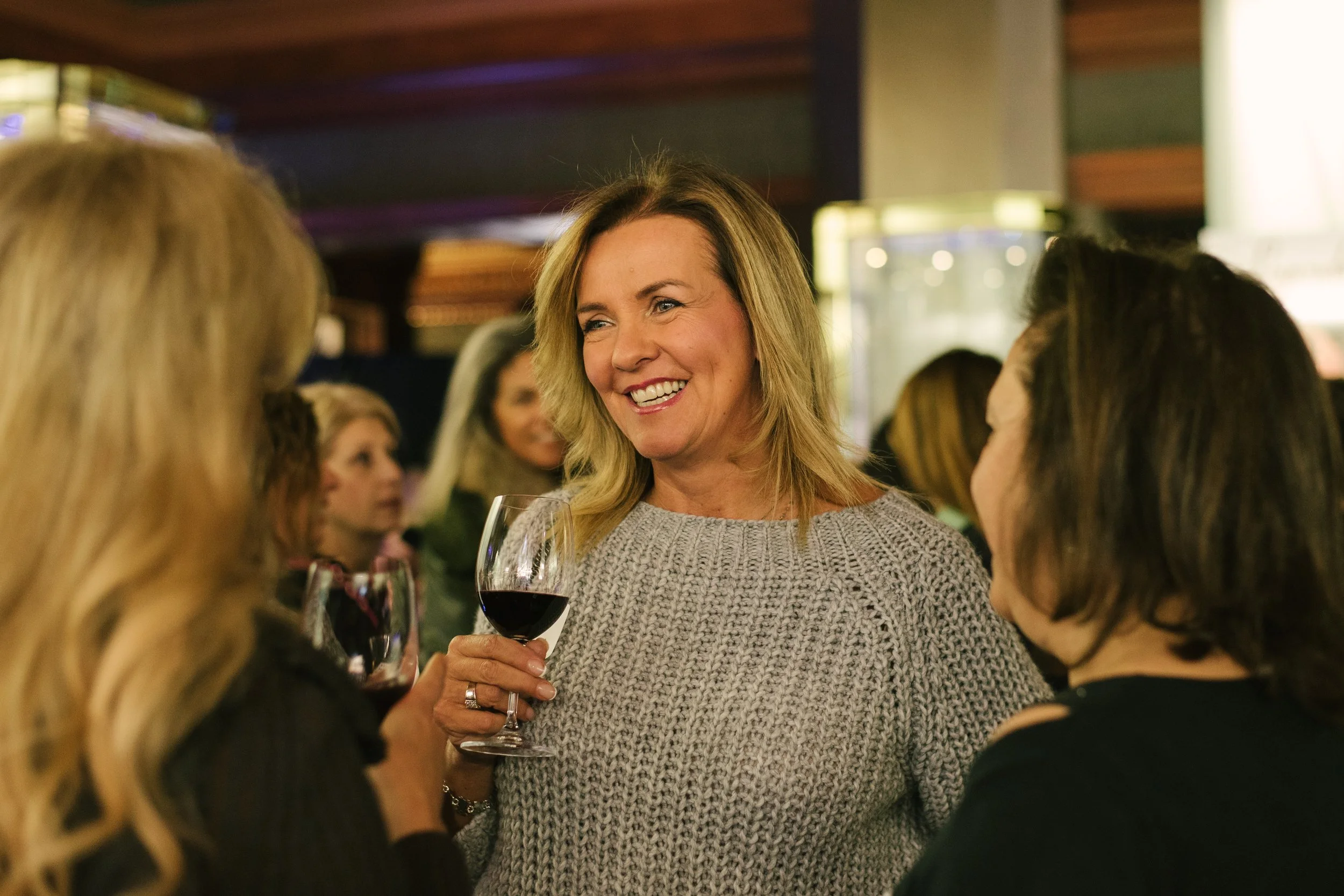 A group of people socializing at corporate event in Toronto with one woman holding a glass of red wine and smiling.