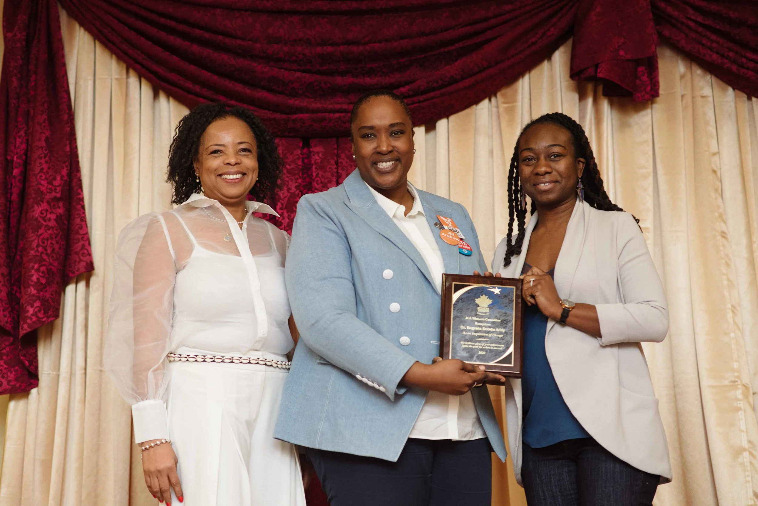 Three women standing on stage in presenting Jill Andrew with an award in Toronto.