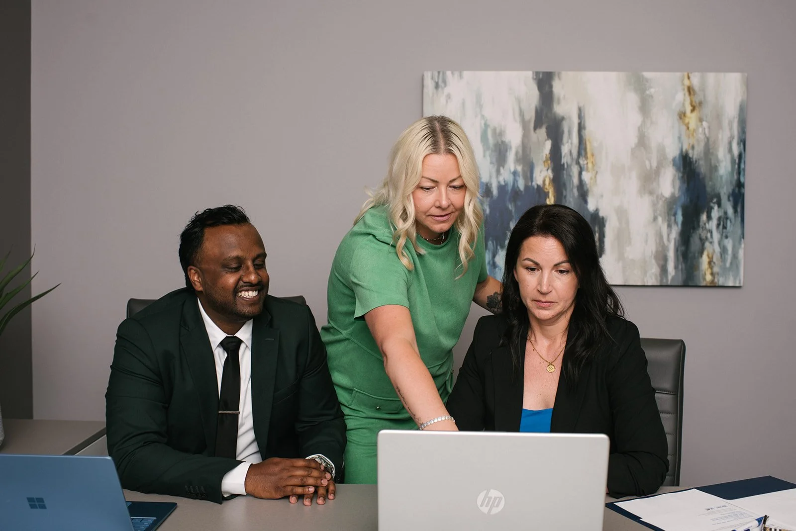 Three business professionals, gathered around a laptop in a modern office, collaborating on work.