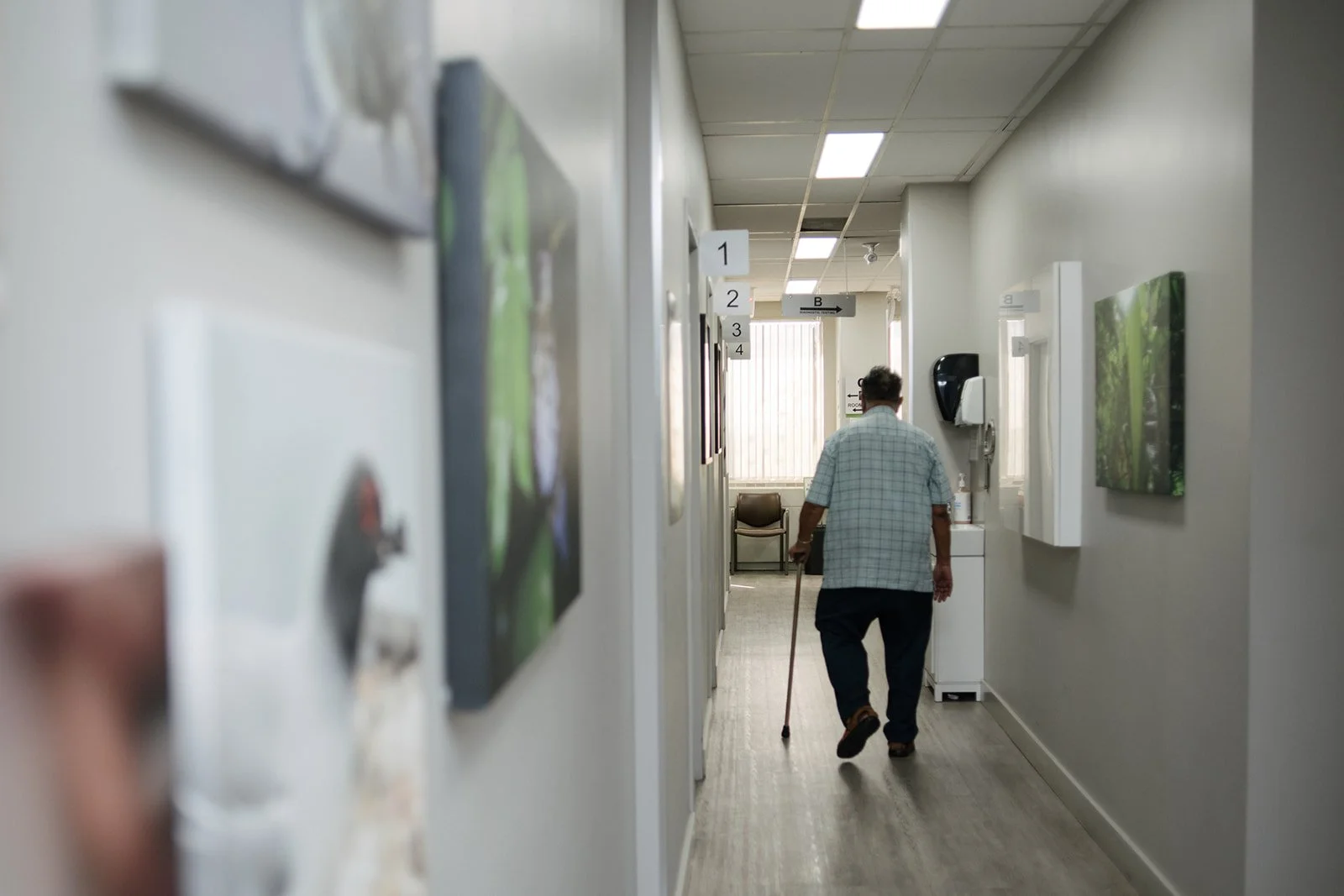 An elderly man with a cane walking down a office corridor.