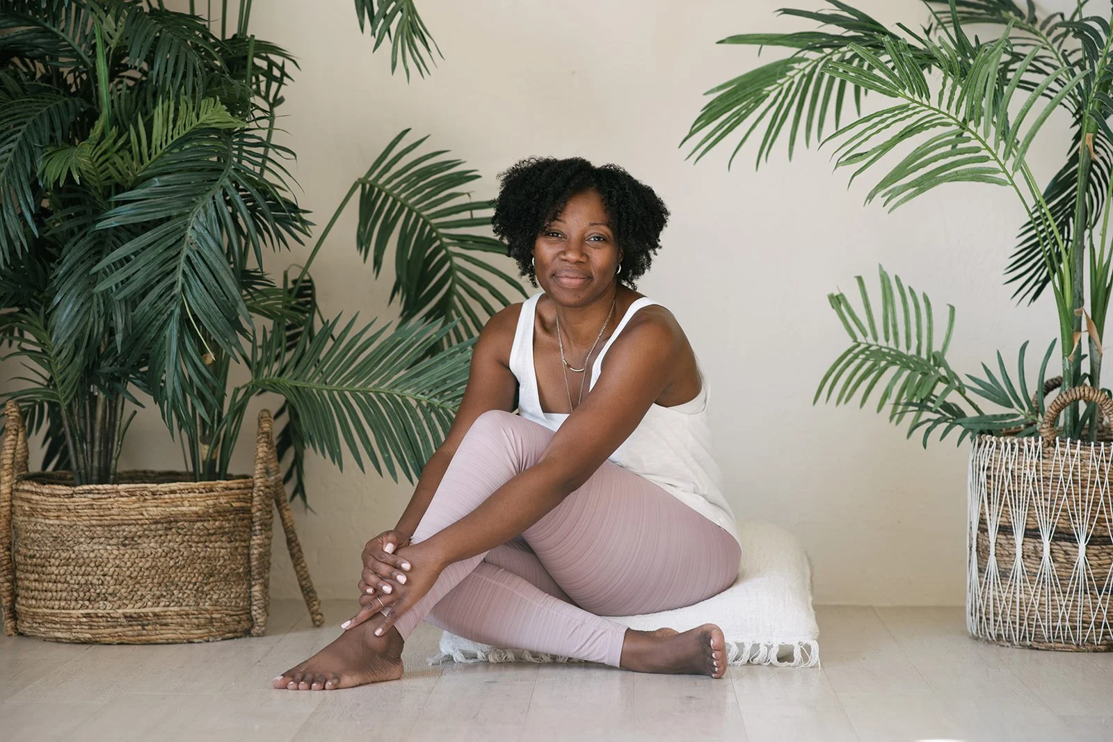A woman sitting on a cushion among potted green plants, smiling at the camera in Mint Room Studios in Toronto.