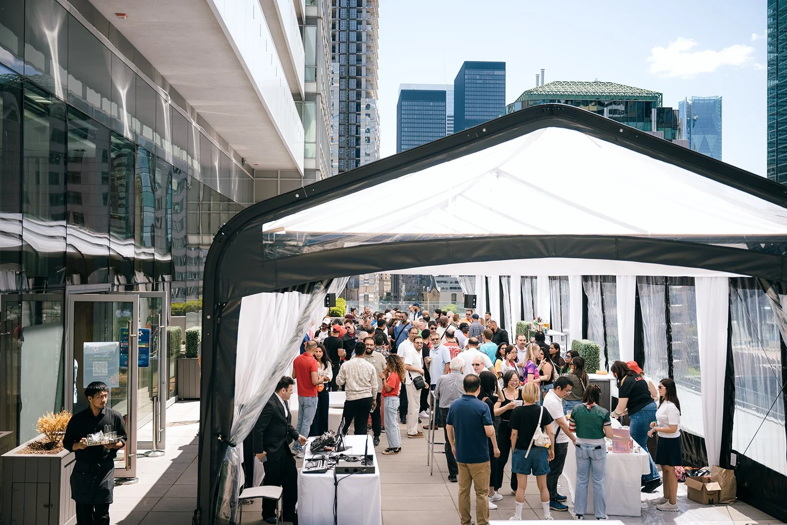 Employees attending an outdoor, corporate event on a terrace surrounded by Toronto skyscrapers, with some tables and a canopy.
