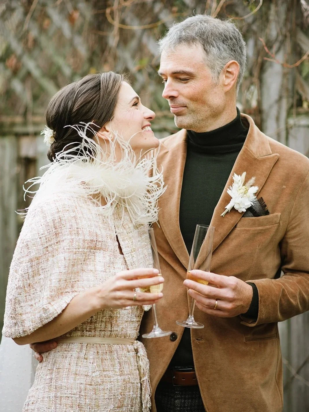 A man and woman at a wedding celebration, gazing at each other while holding champagne glasses.