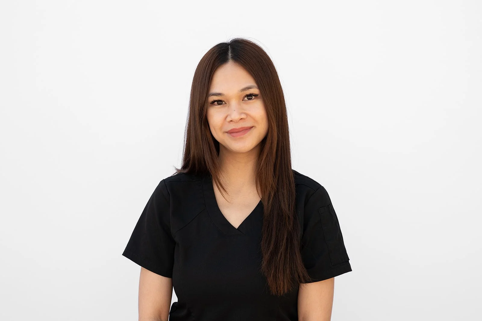 A headshot of a young woman with long brown hair wearing a black shirt, smiling softly at the camera against a plain white background.