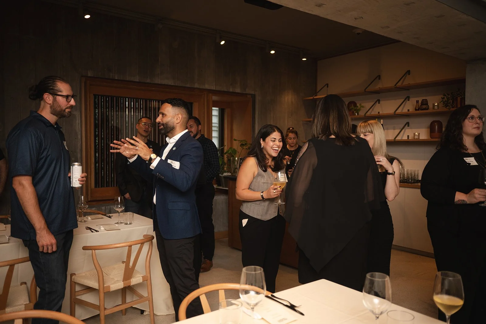 People socializing at a wine tasting event in a modern restaurant or lounge, some holding wine glasses and engaging in conversations.