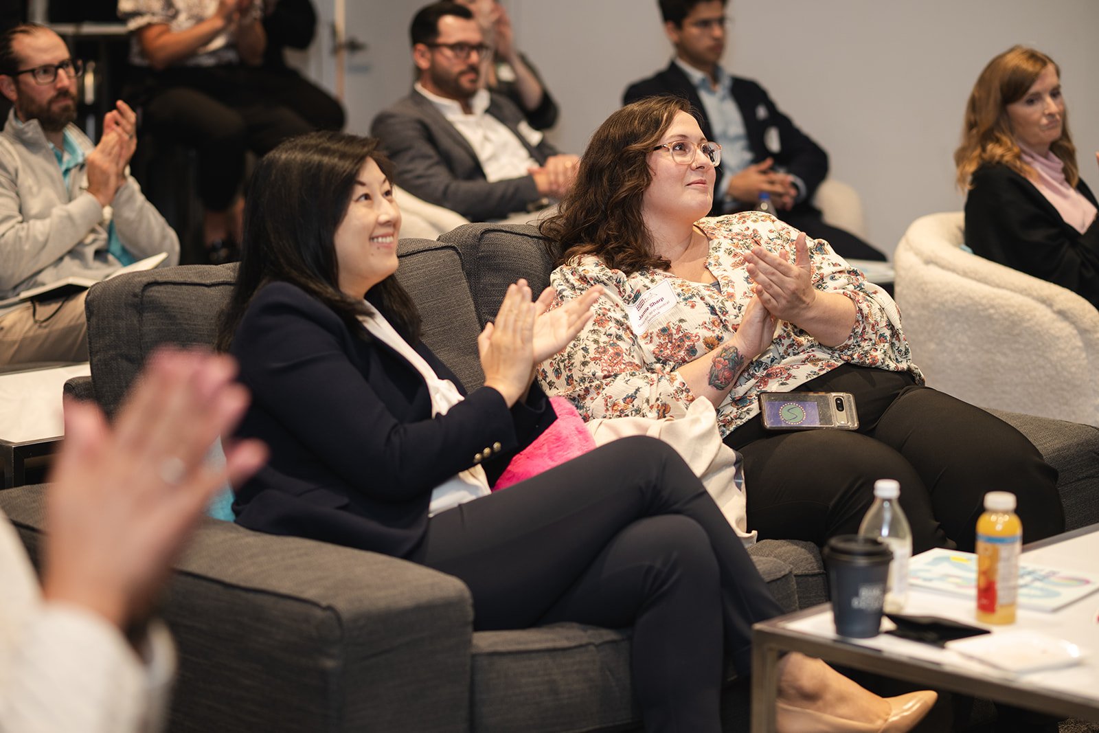 People seated on couches and chairs at a professional corporate event, applauding.