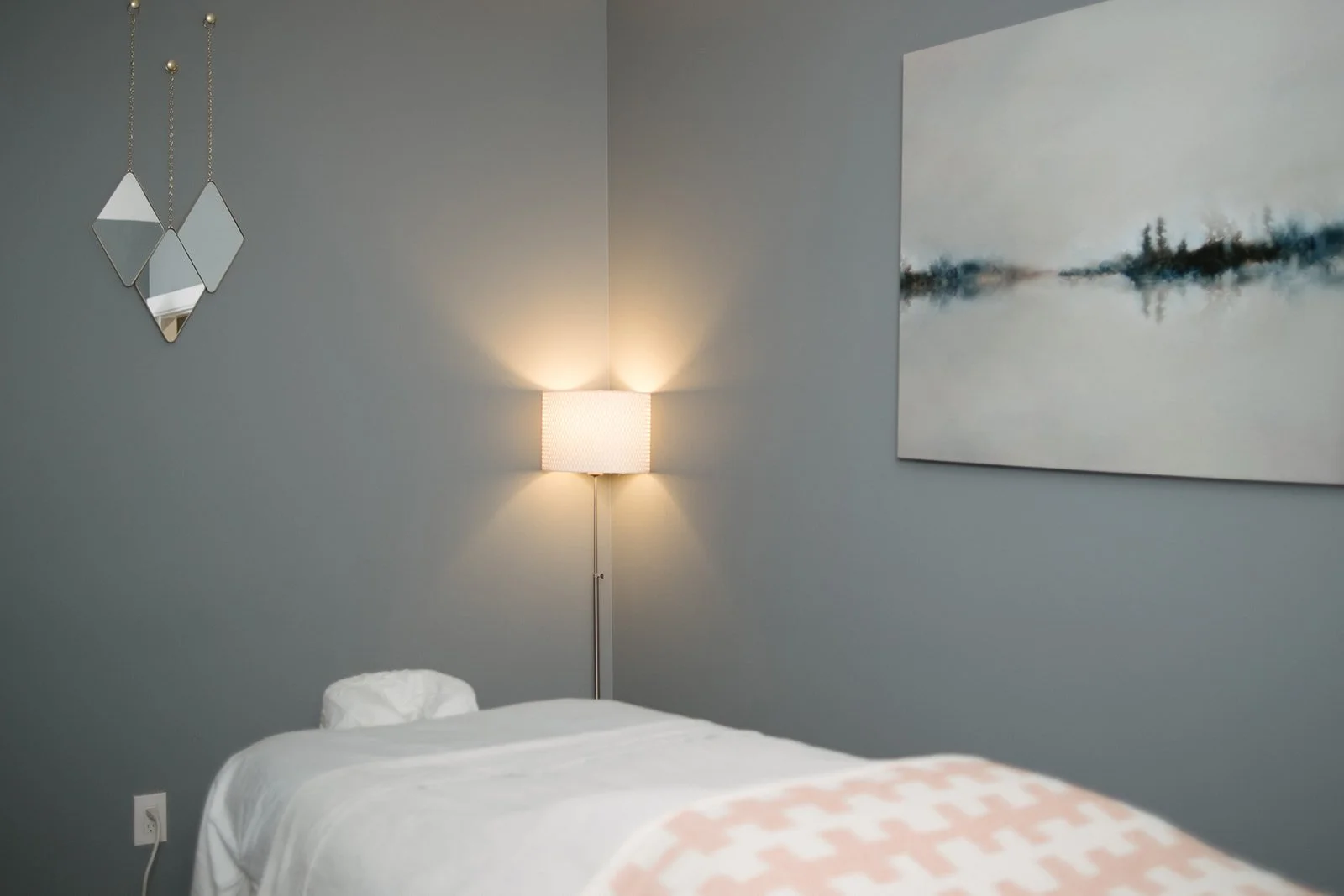 A room filled with a massage table, wall art, and a floor lamp emitting warm light.