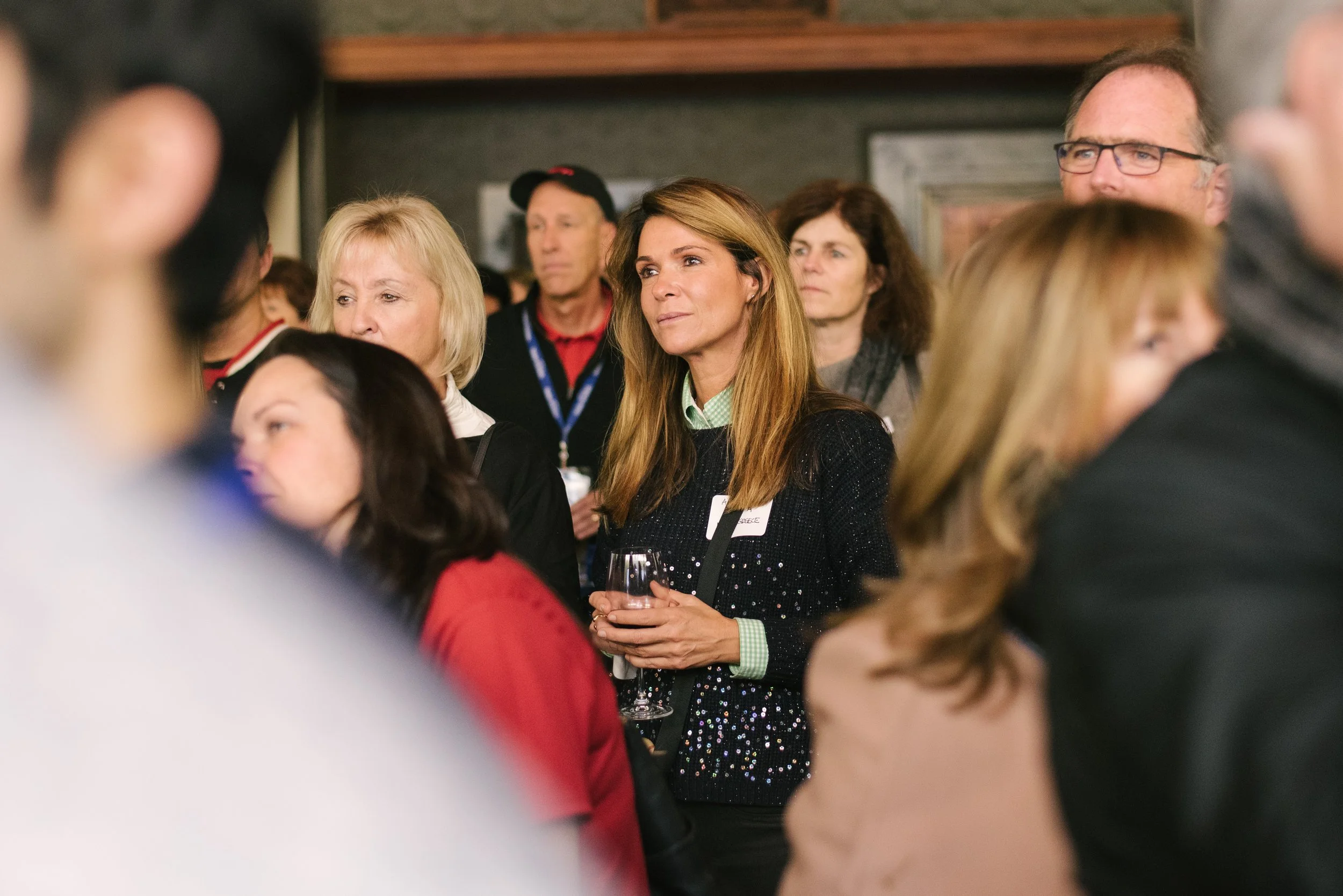 A group of people attending a professional corporate event, with one woman in the centre holding listening attentively.