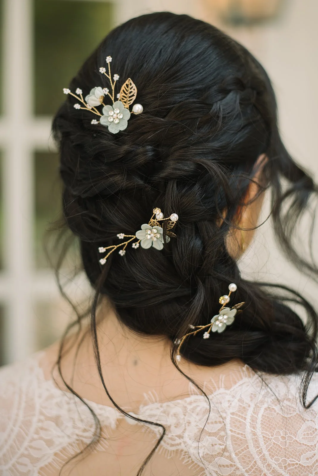 Up-do hairstyle with black hair decorated with floral headpieces containing white flowers, pearls, and gold leaves.