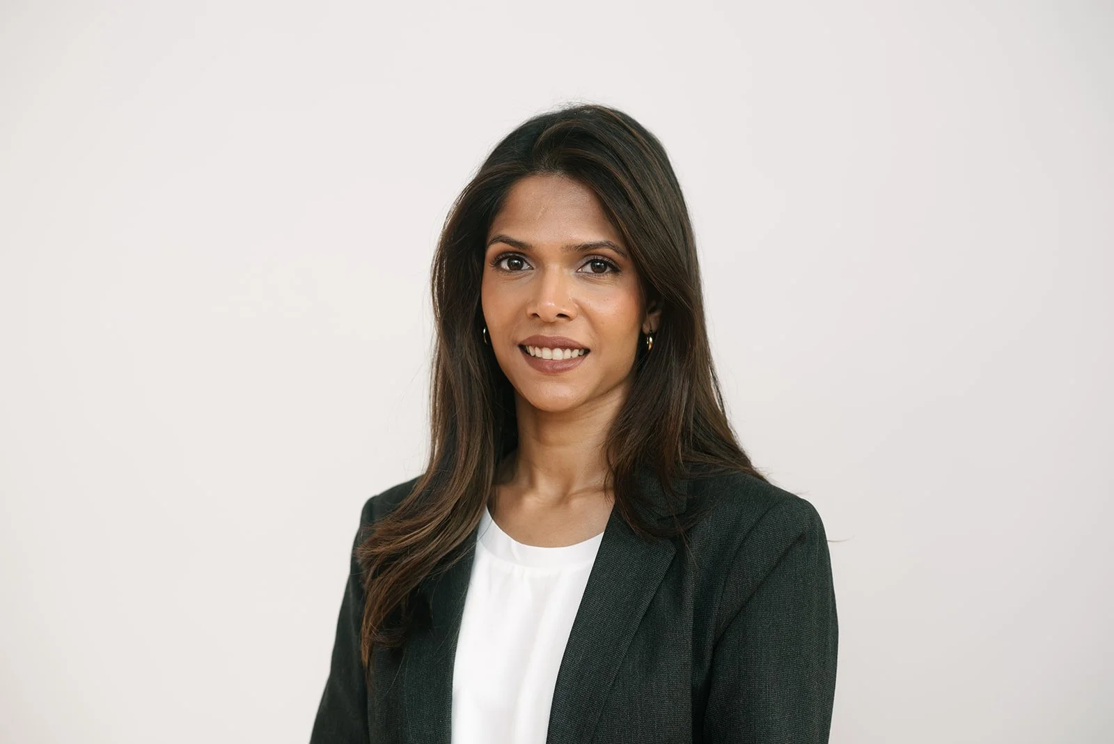 A professional woman with long dark hair wearing a black blazer and white blouse, standing against a plain white background.