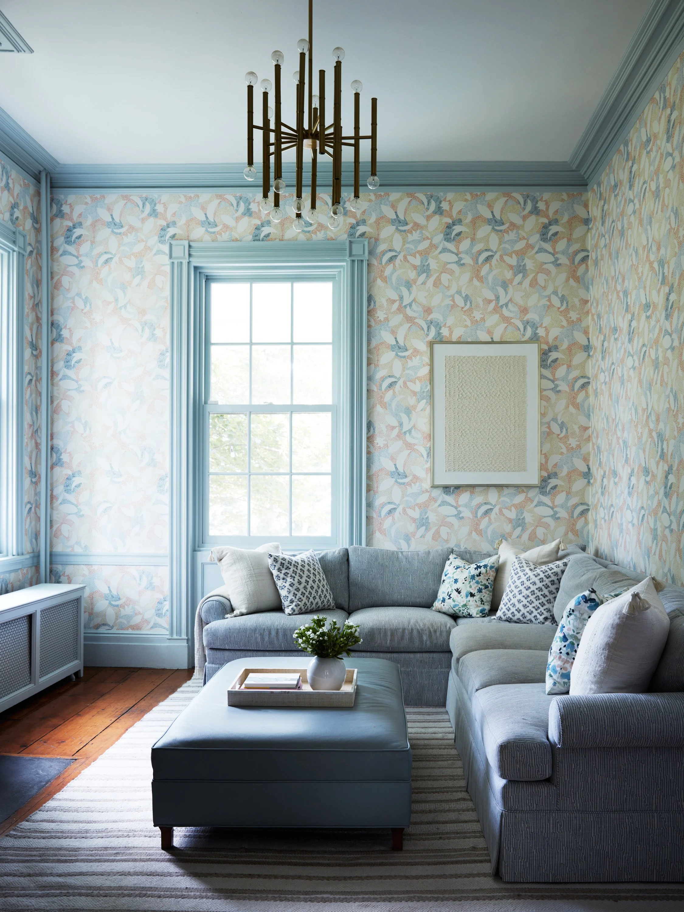 Classic home renovation in Bronxville featuring light blue painted molding, elegant floral wallpaper, and modern, comfortable seating that honors the original architecture.