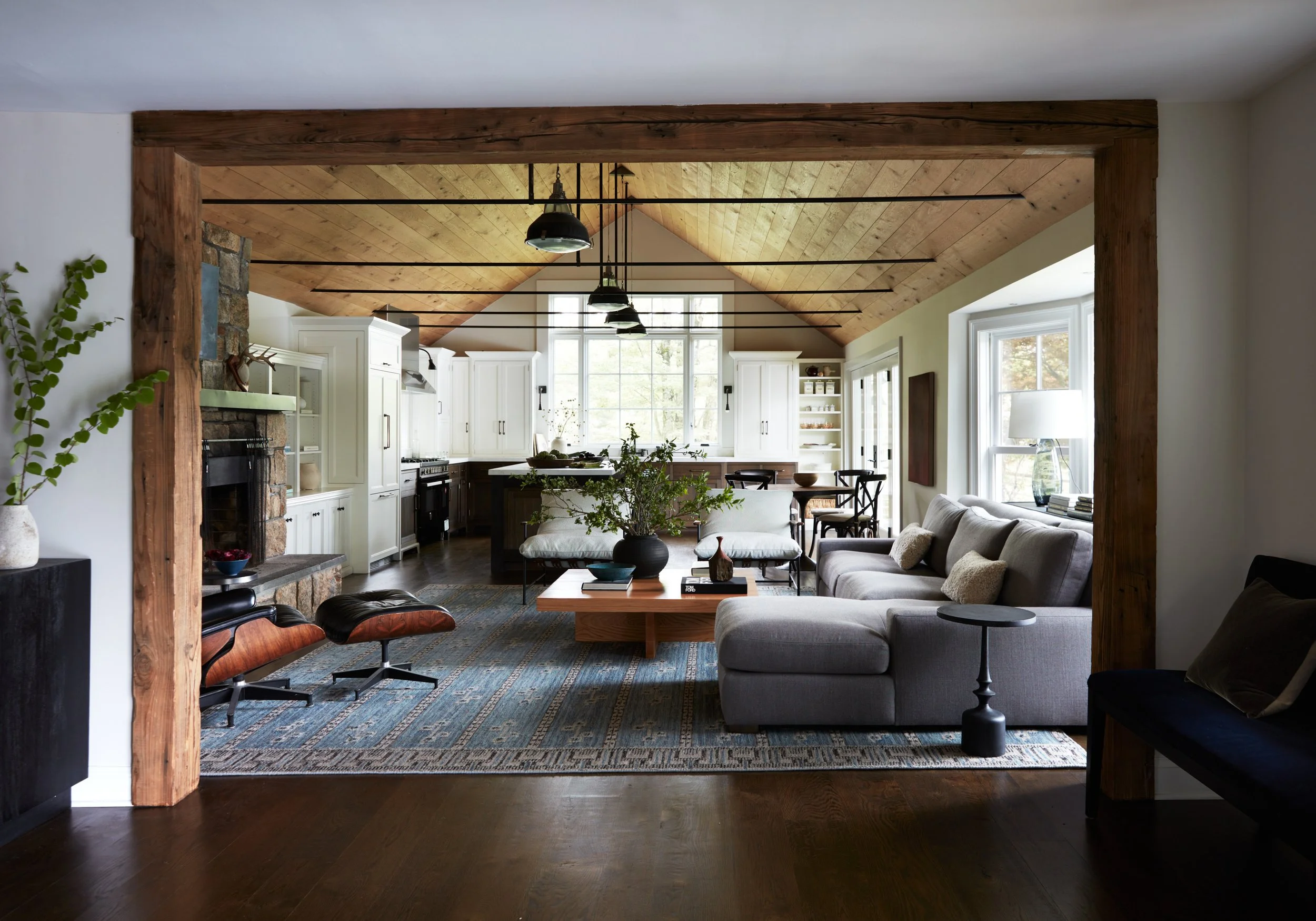 Open kitchen and living room with exposed timber framing, a vaulted wood ceiling, custom cabinetry, and integrated seating areas.