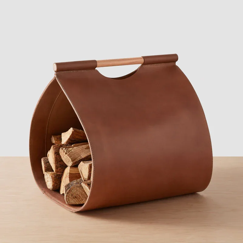 The Citizenry brown leather firewood log holder filled with stacked logs, styled near a fireplace in a home, showcasing warm, elevated interior design posted on a blog by a Westchester interior design studio - Barrett Oswald Designs.