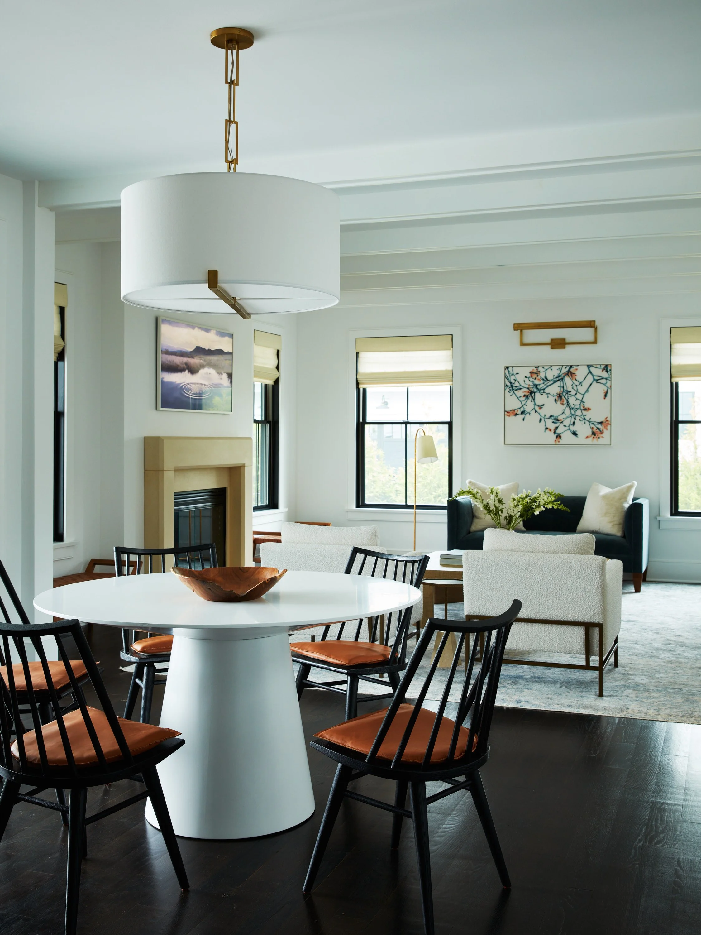 Open dining and living area with round white table black chairs and sculptural pendant lighting