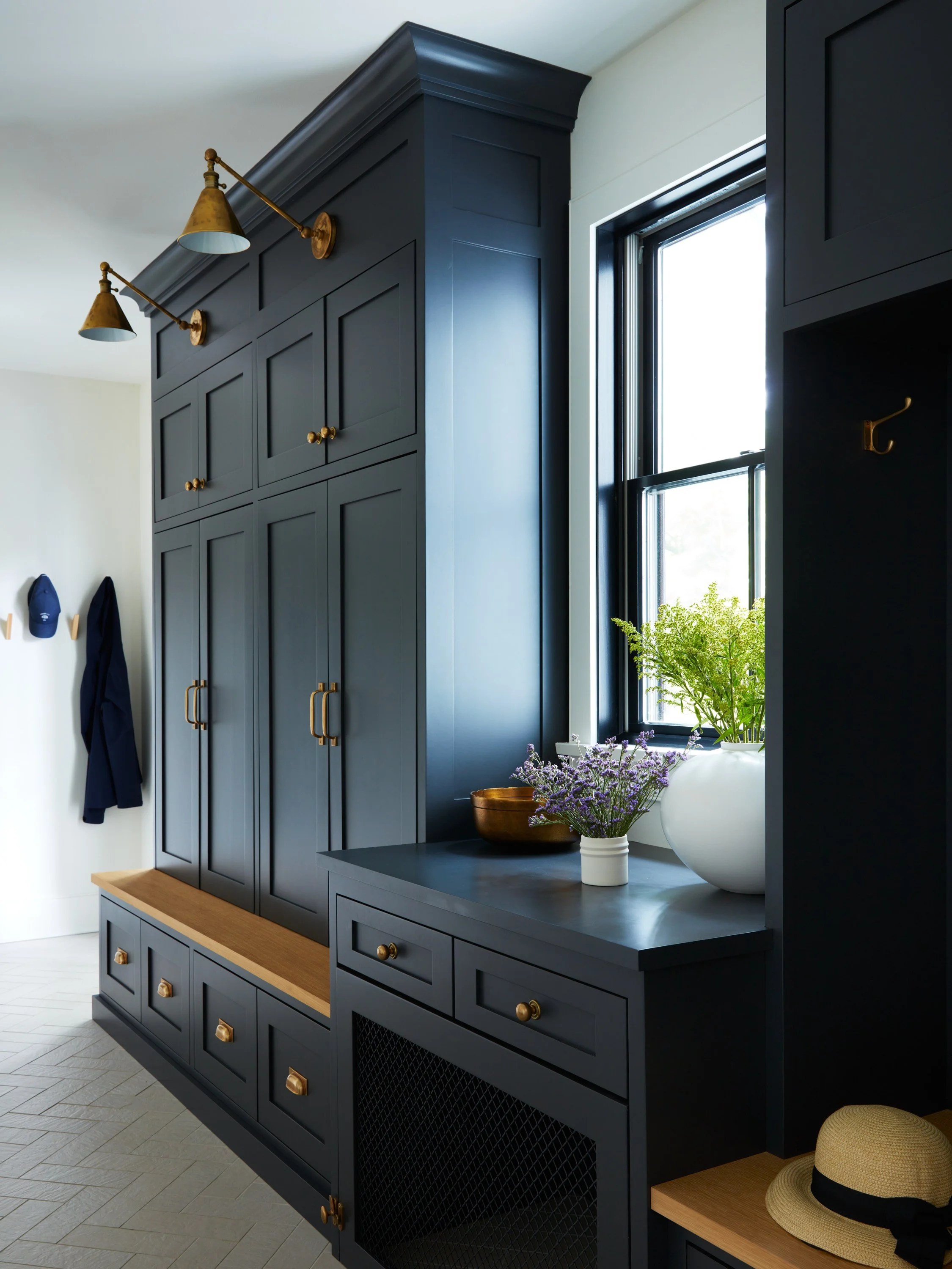 Functional and stylish mudroom design in Scarsdale, NY, featuring custom dark millwork cabinetry, brass hardware, and built-in bench seating for a busy family.