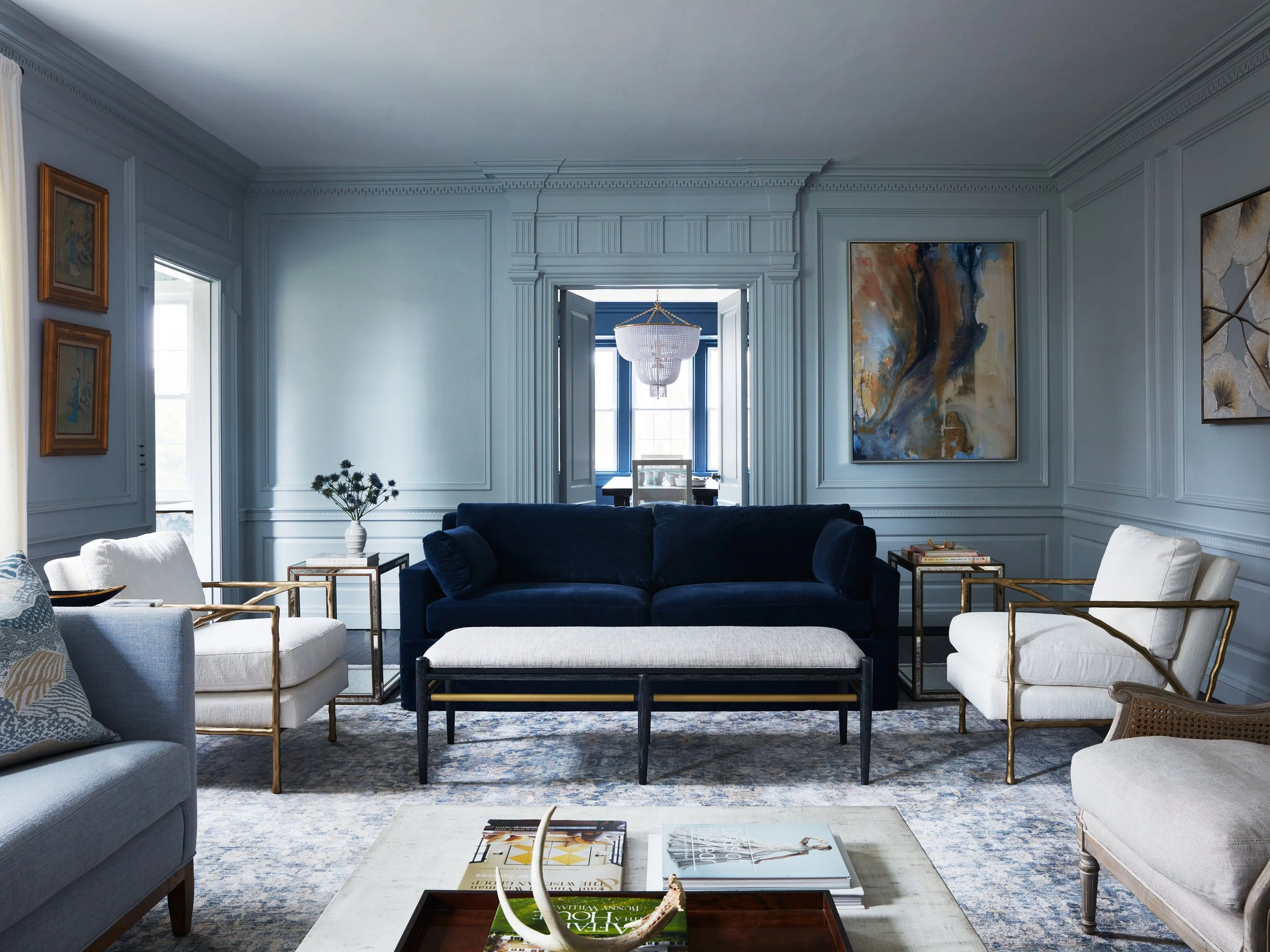 Blue paneled North Salem living room with custom millwork, a navy velvet sofa, and views into the adjoining room.