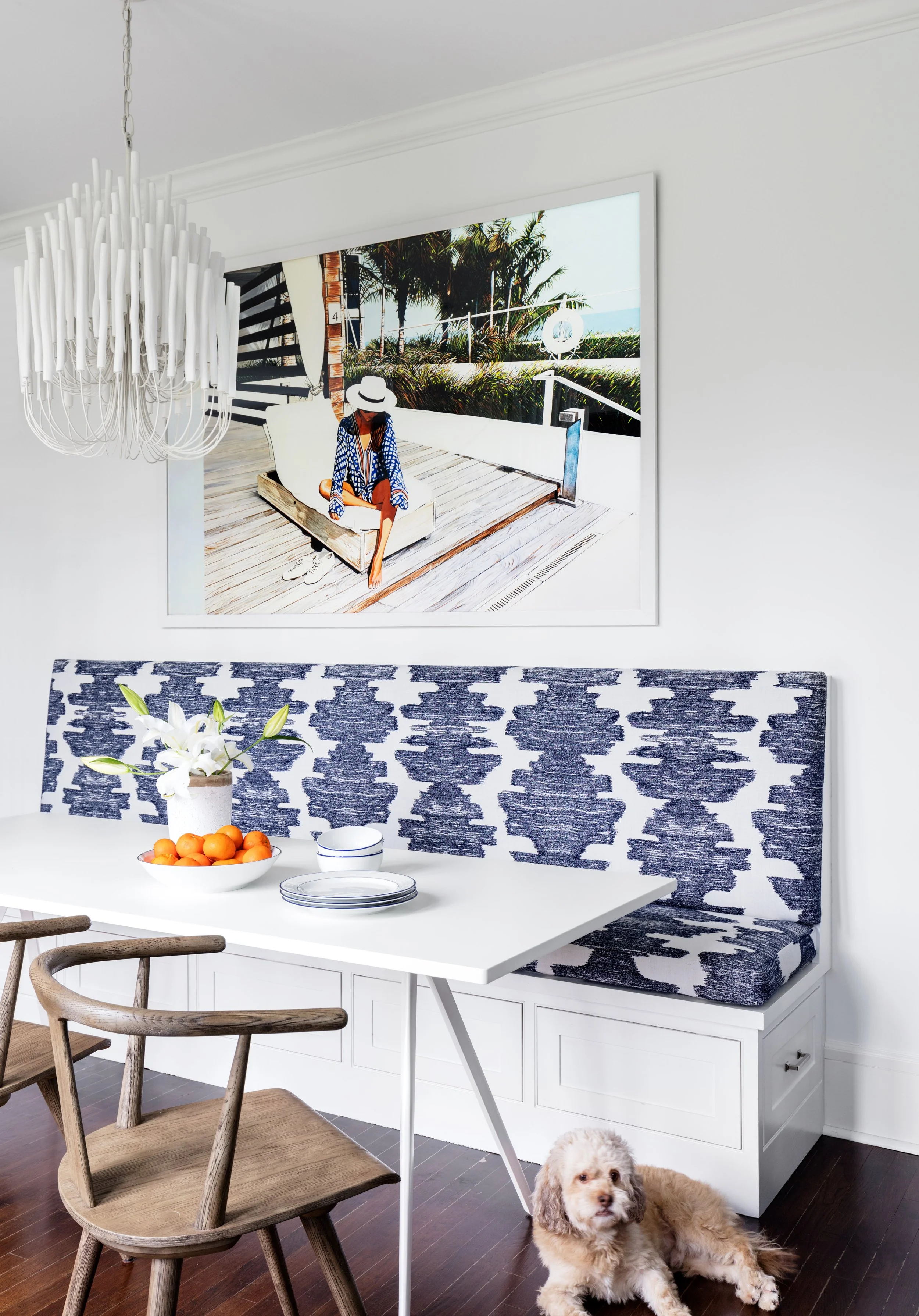Breakfast nook with blue upholstered bench white table wood chairs and large scale artwork