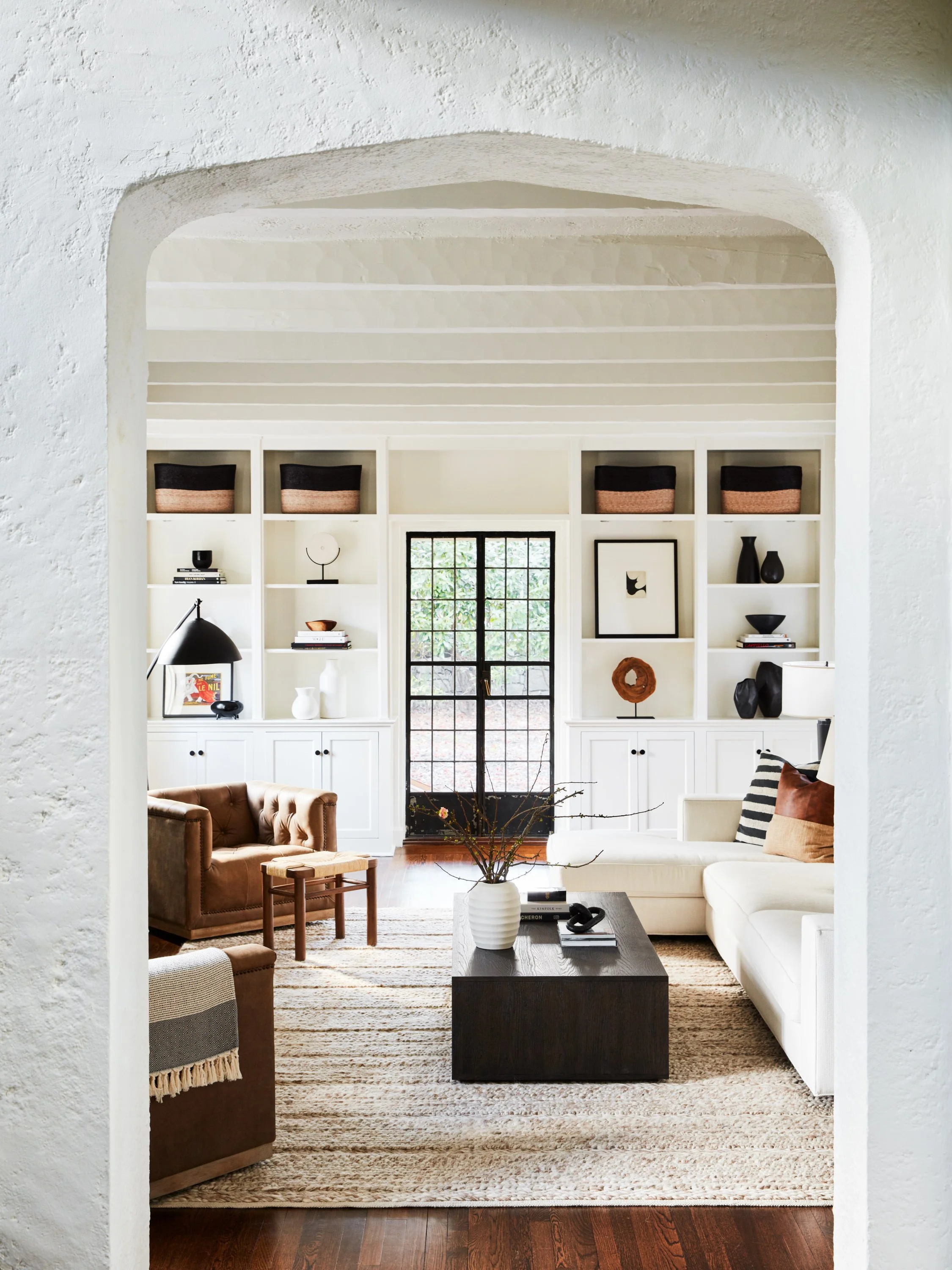 Living room framed by archway with white built ins neutral sofa and textured rug