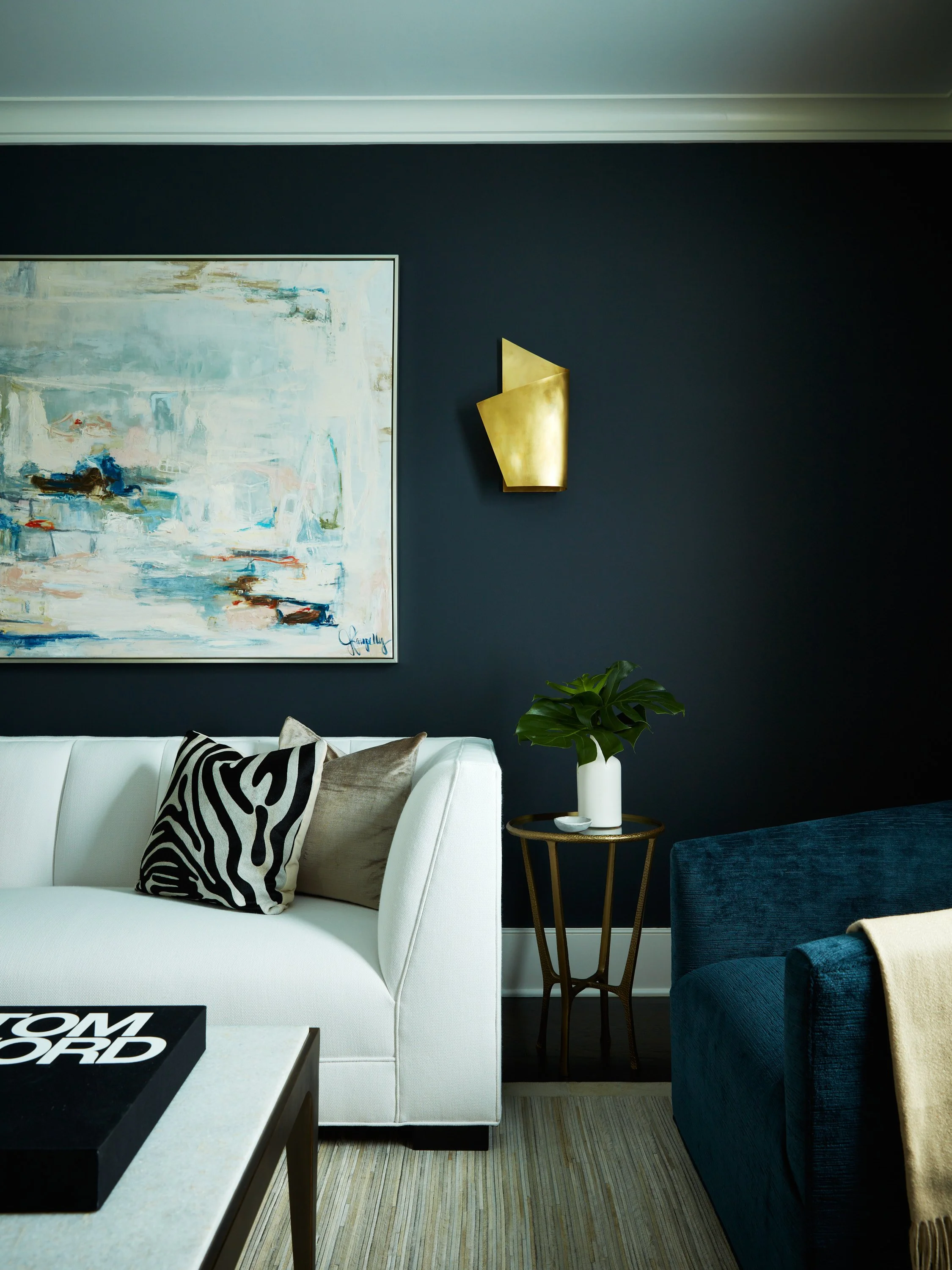 Moody navy living room with zebra print pillow, brass wall sconce, and modern artwork creating a layered, refined interior in Westchester, NY