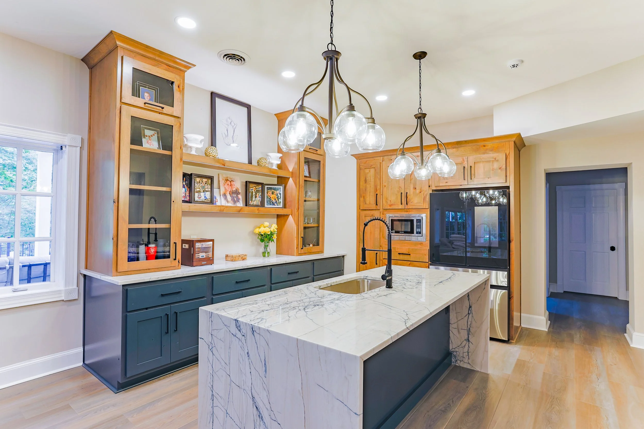 Modern kitchen with a marble island, wooden cabinets, black fixtures, and decorative lighting.