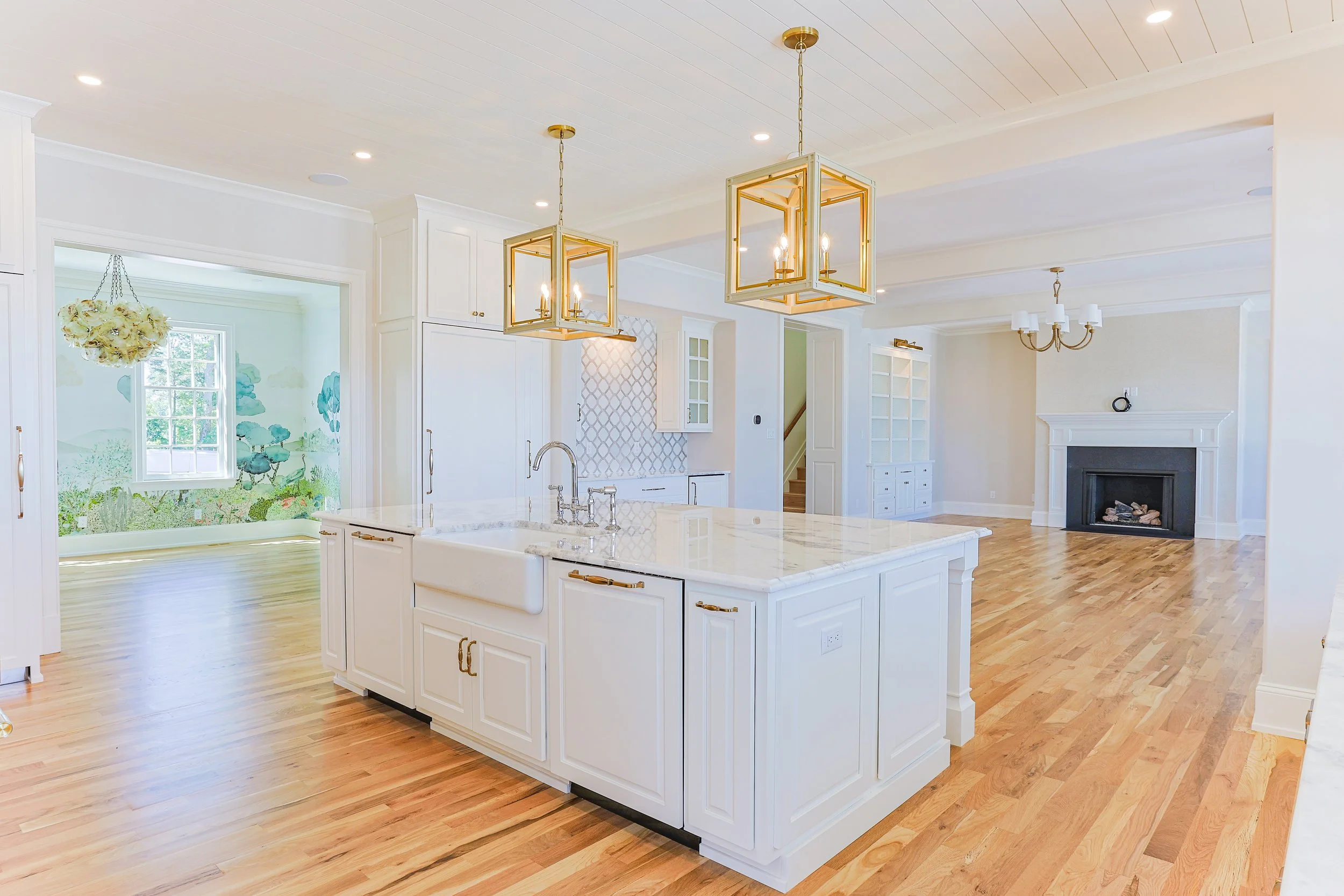 Bright, spacious kitchen with white cabinets, marble island, wooden flooring, and a fireplace in the living area.