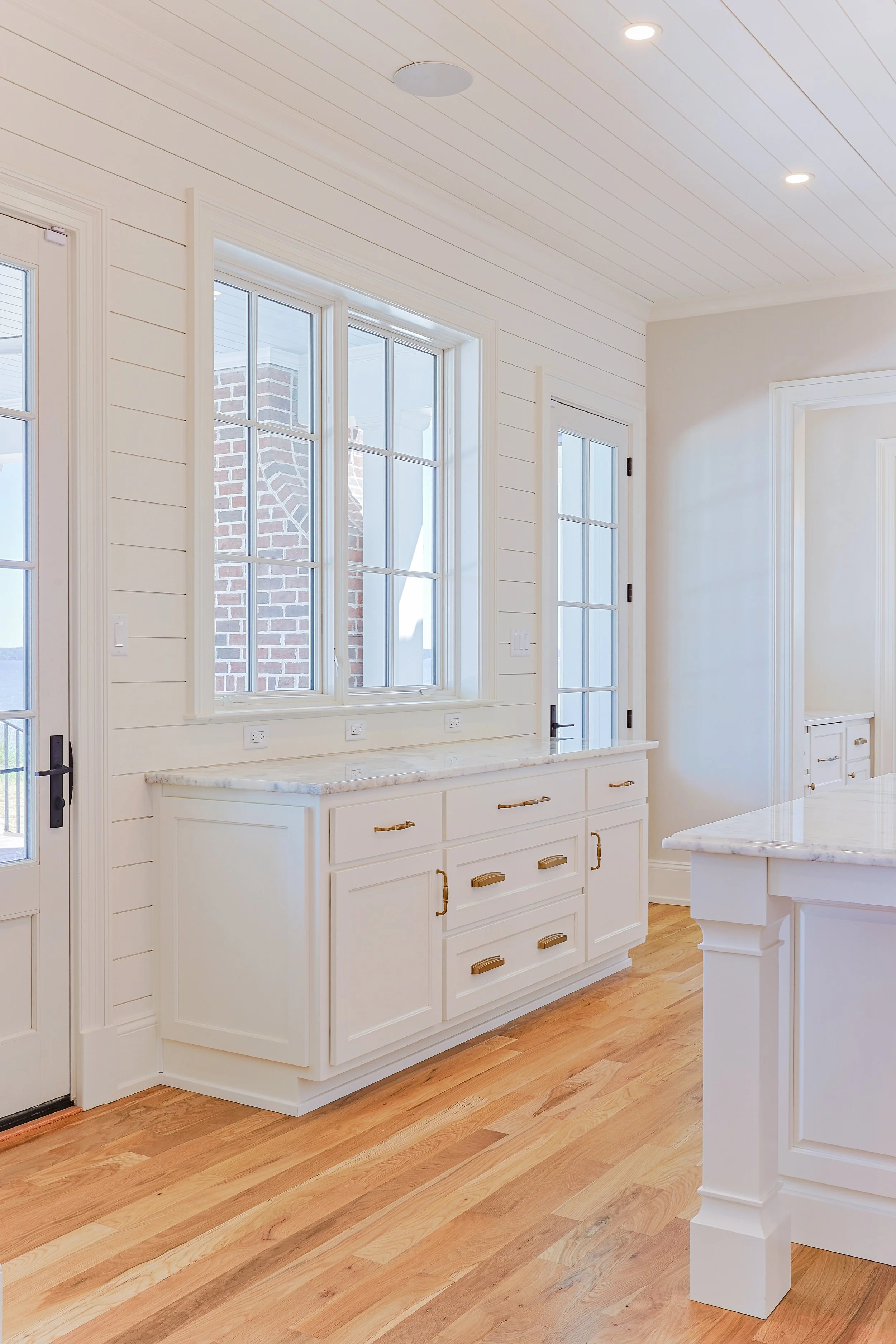 Bright kitchen with white cabinets, granite countertops, wooden floors, and large windows.
