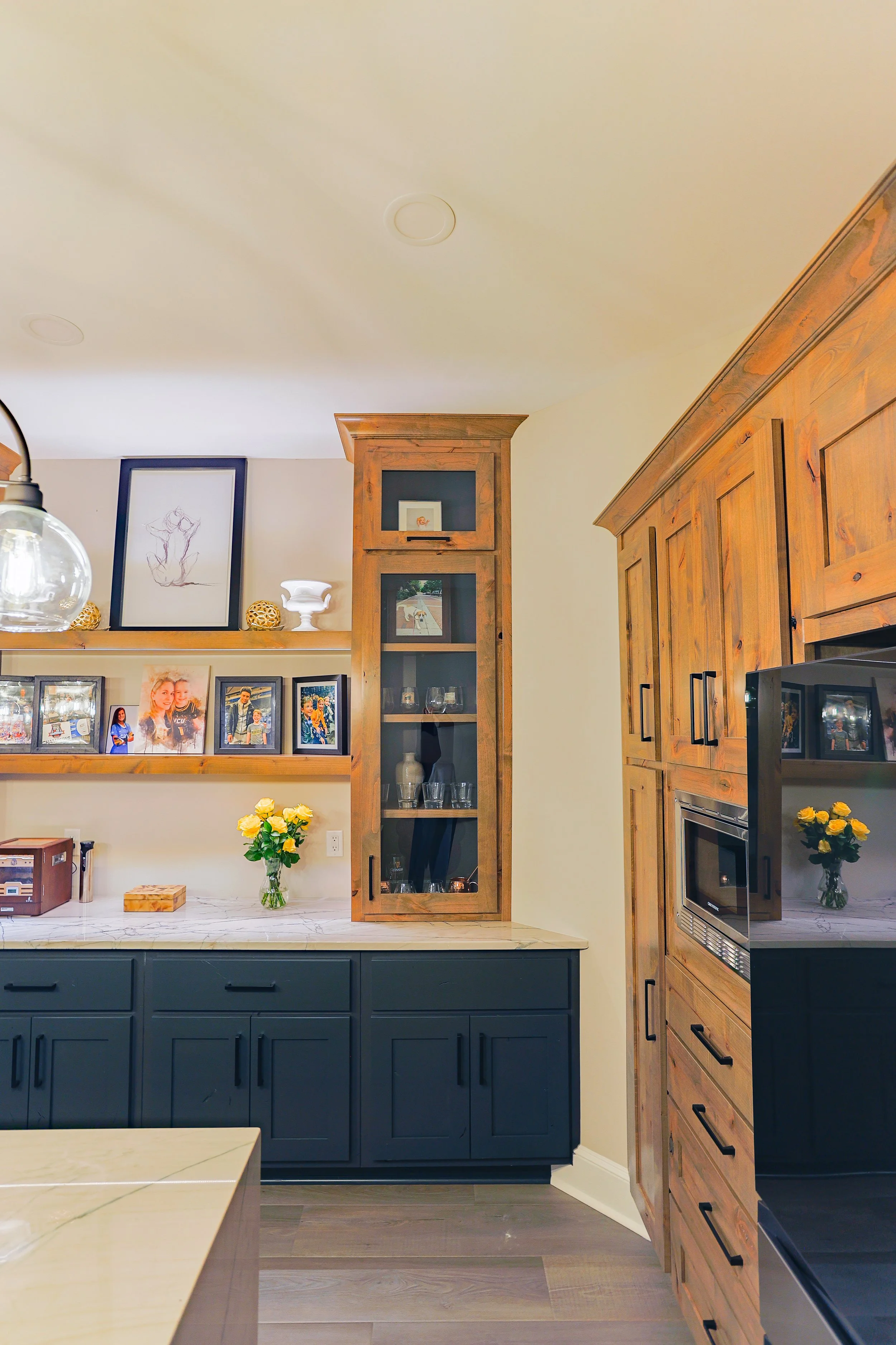 Kitchen with wooden cabinets, a marble countertop, framed family photos, a flower vase, and decorative items on shelves.