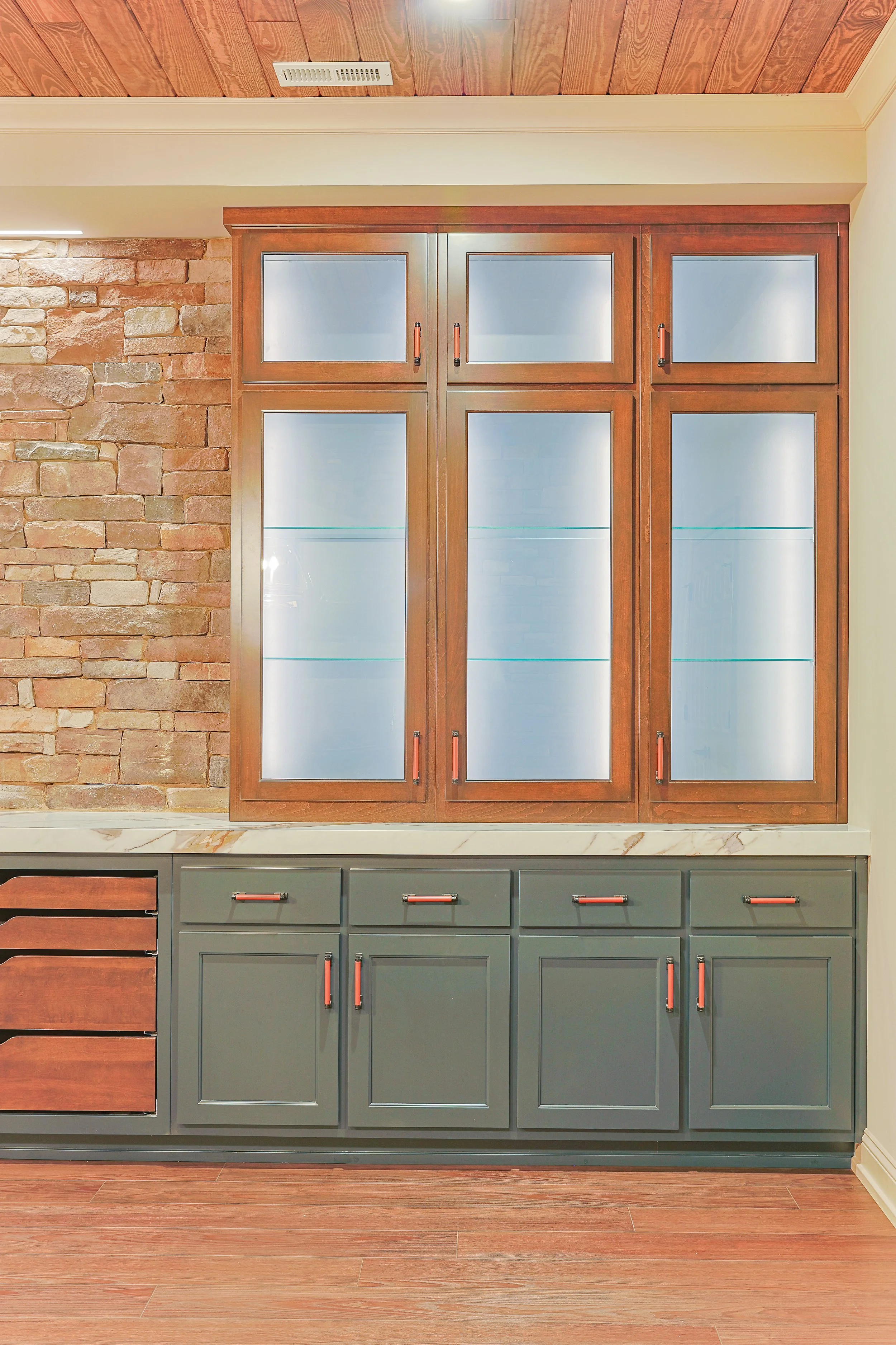 A built-in cabinet with glass doors and wooden frames, situated against a brick wall with a white crown molding and ceiling panel.