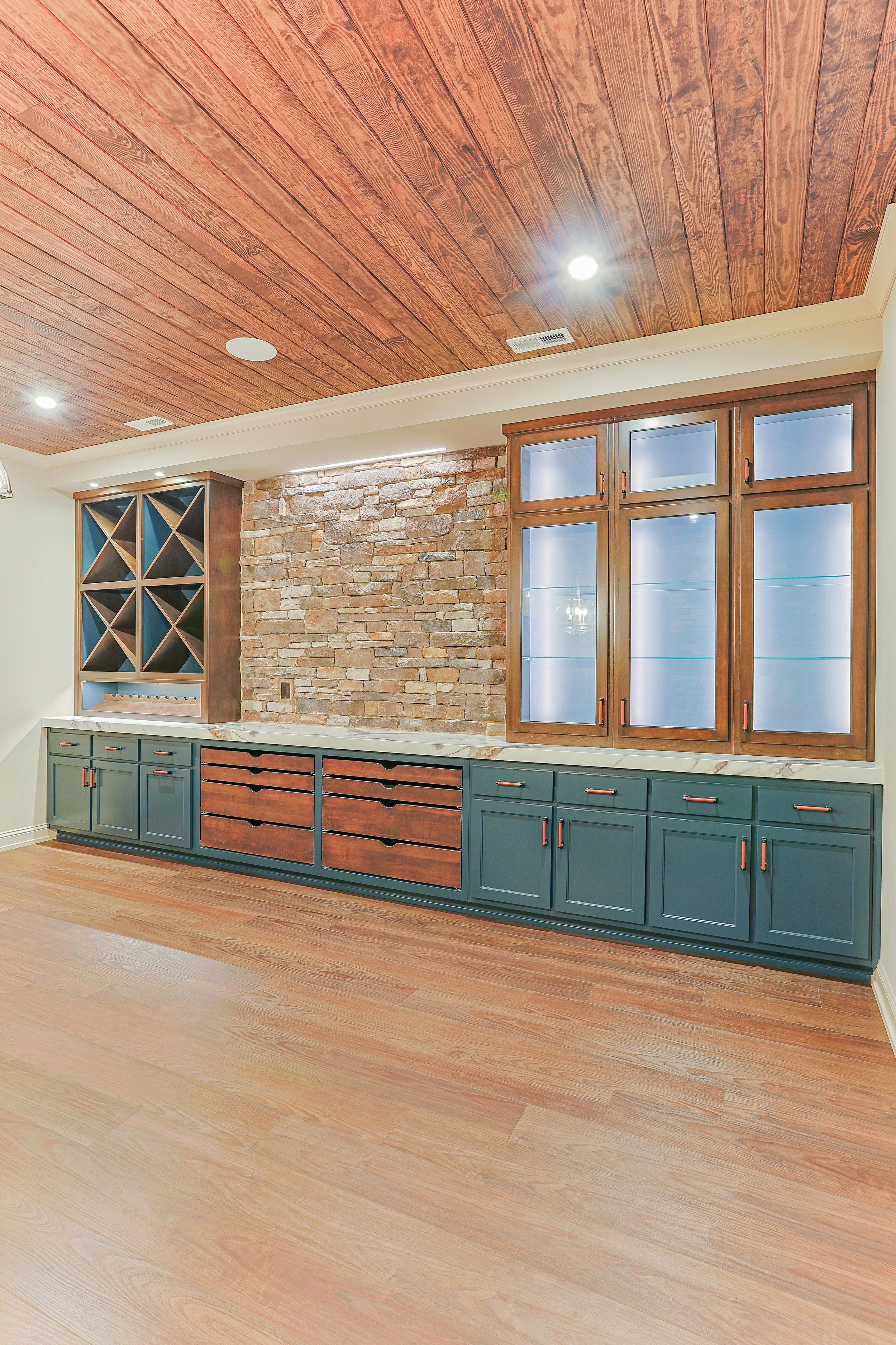 Interior view of a kitchen or entertainment room with wooden ceiling, brick wall, and built-in cabinets with glass doors and drawers.