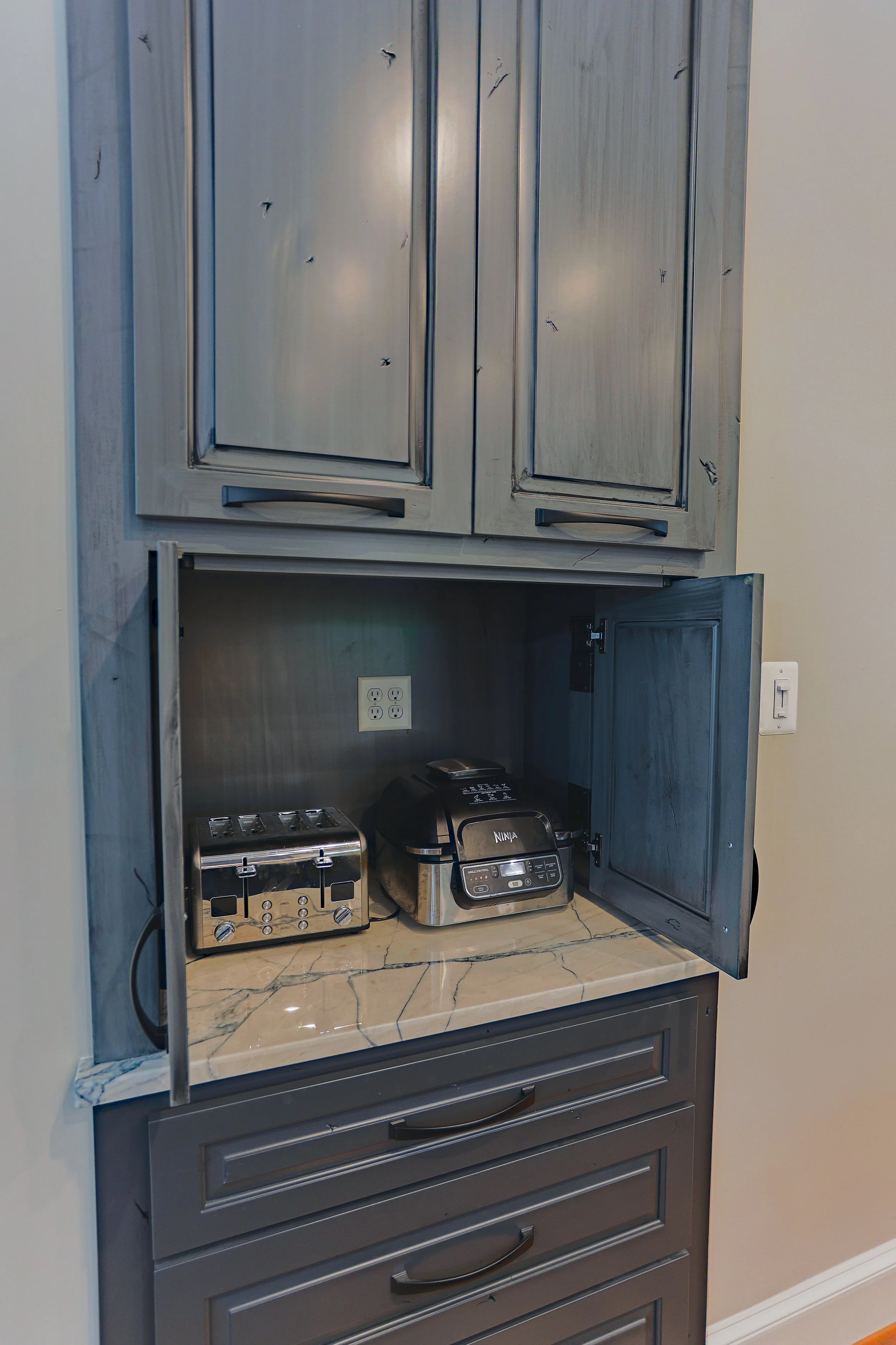 Kitchen cabinet with open doors revealing a toaster, rice cooker, and a wall outlet inside