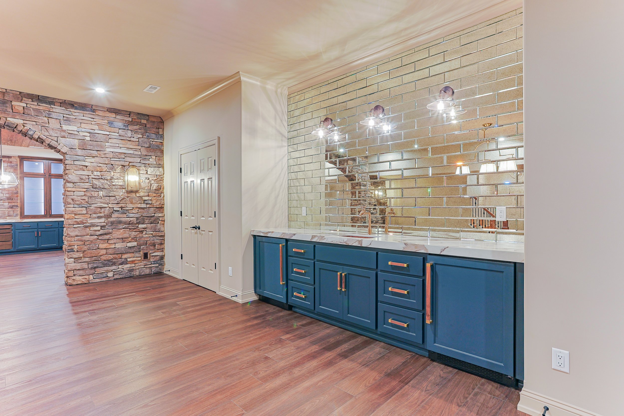 Modern interior room with a blue cabinet, marble countertop, brick wall with a mirror, and wood flooring.