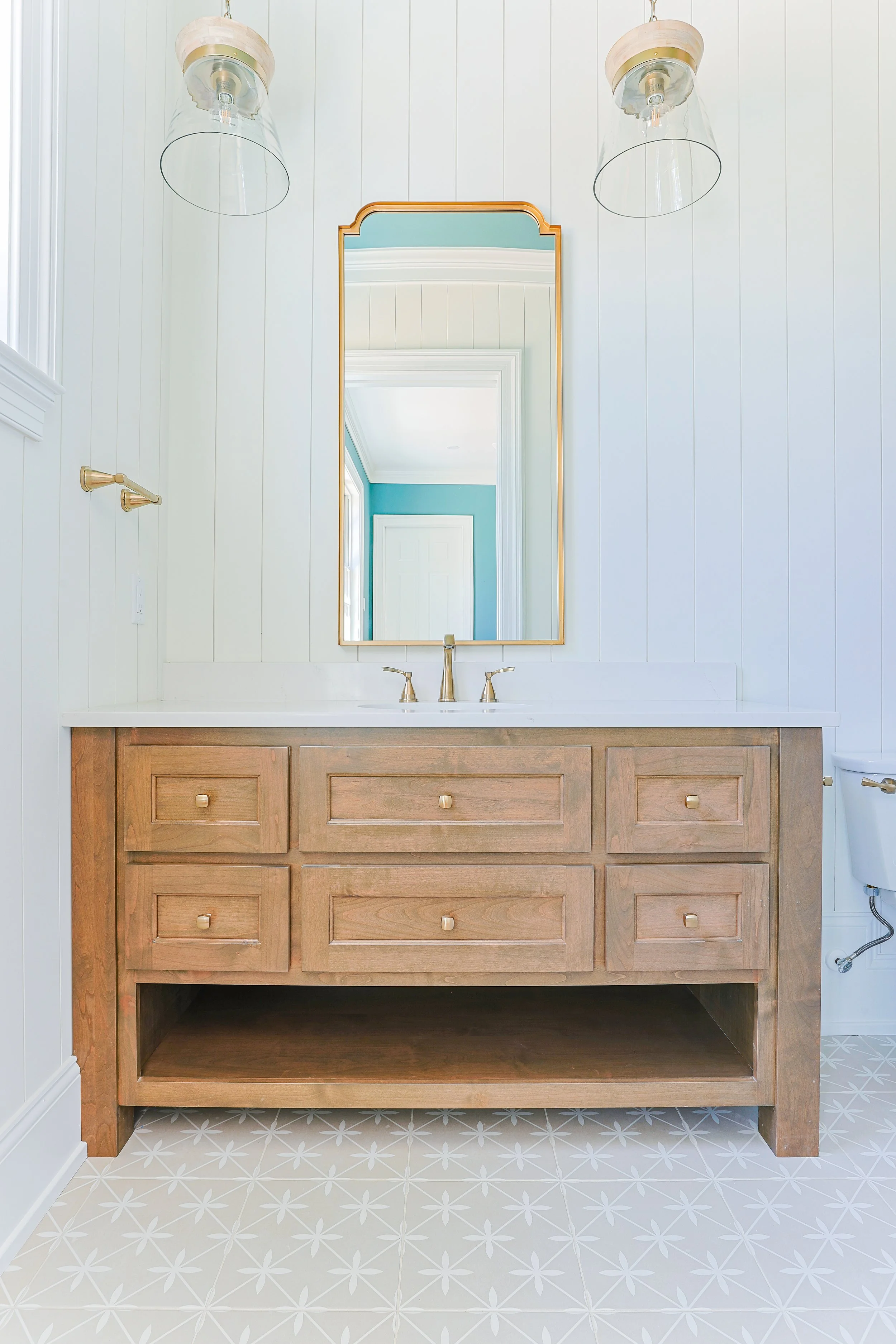 Bathroom vanity with wooden cabinet, white countertop, gold fixtures, and a mirror, with two glass light fixtures above.