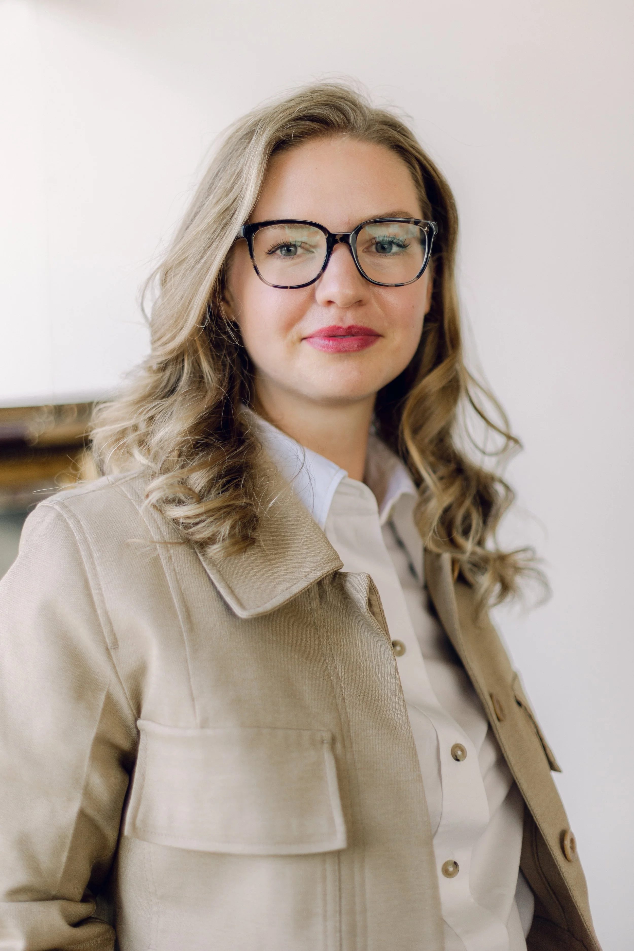 Kate, a white woman with glasses and curly dark blonde hair, looking directly into the camera collaged over a photo of tall grasses