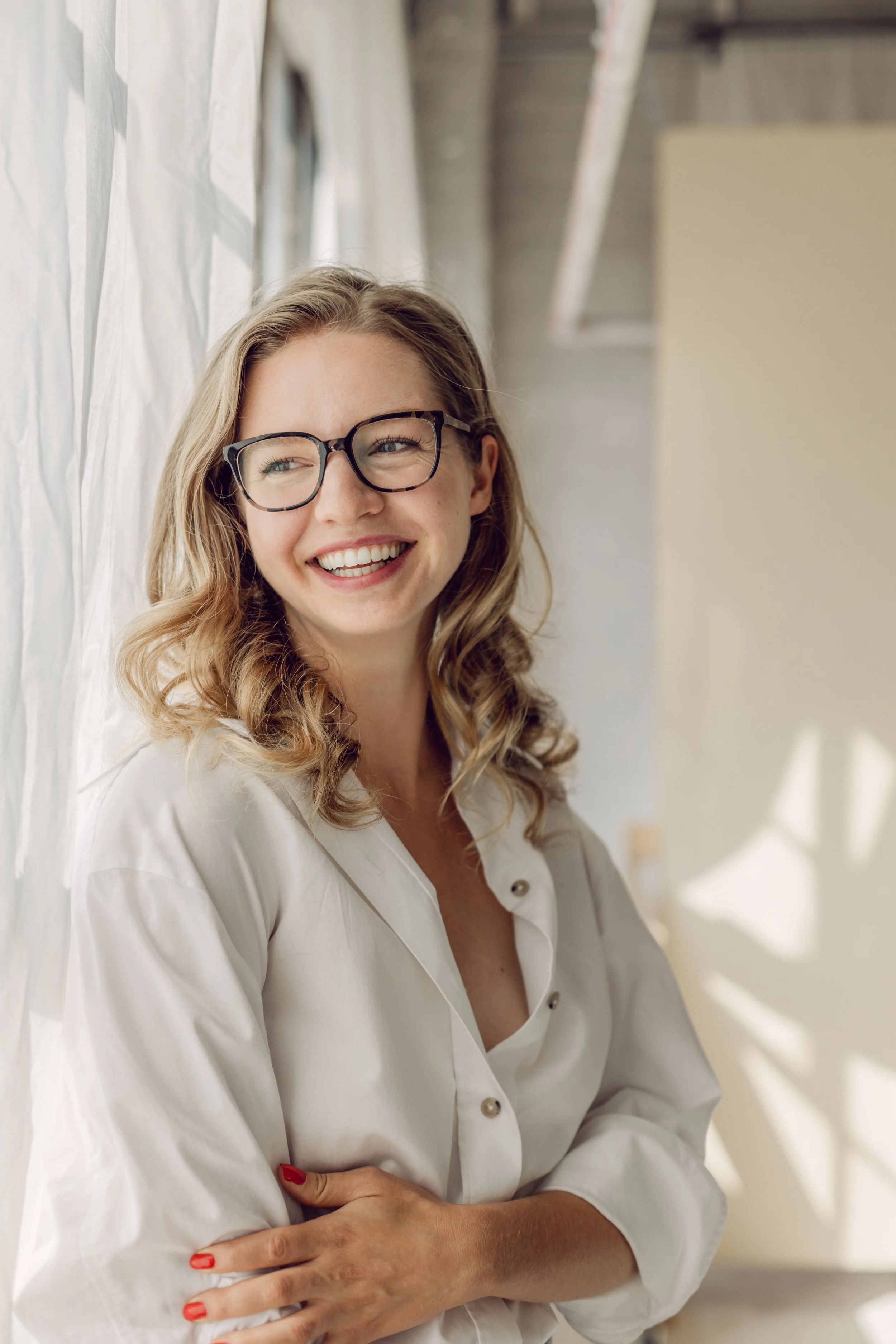 Kate smiles widely in front of a sunny loft window