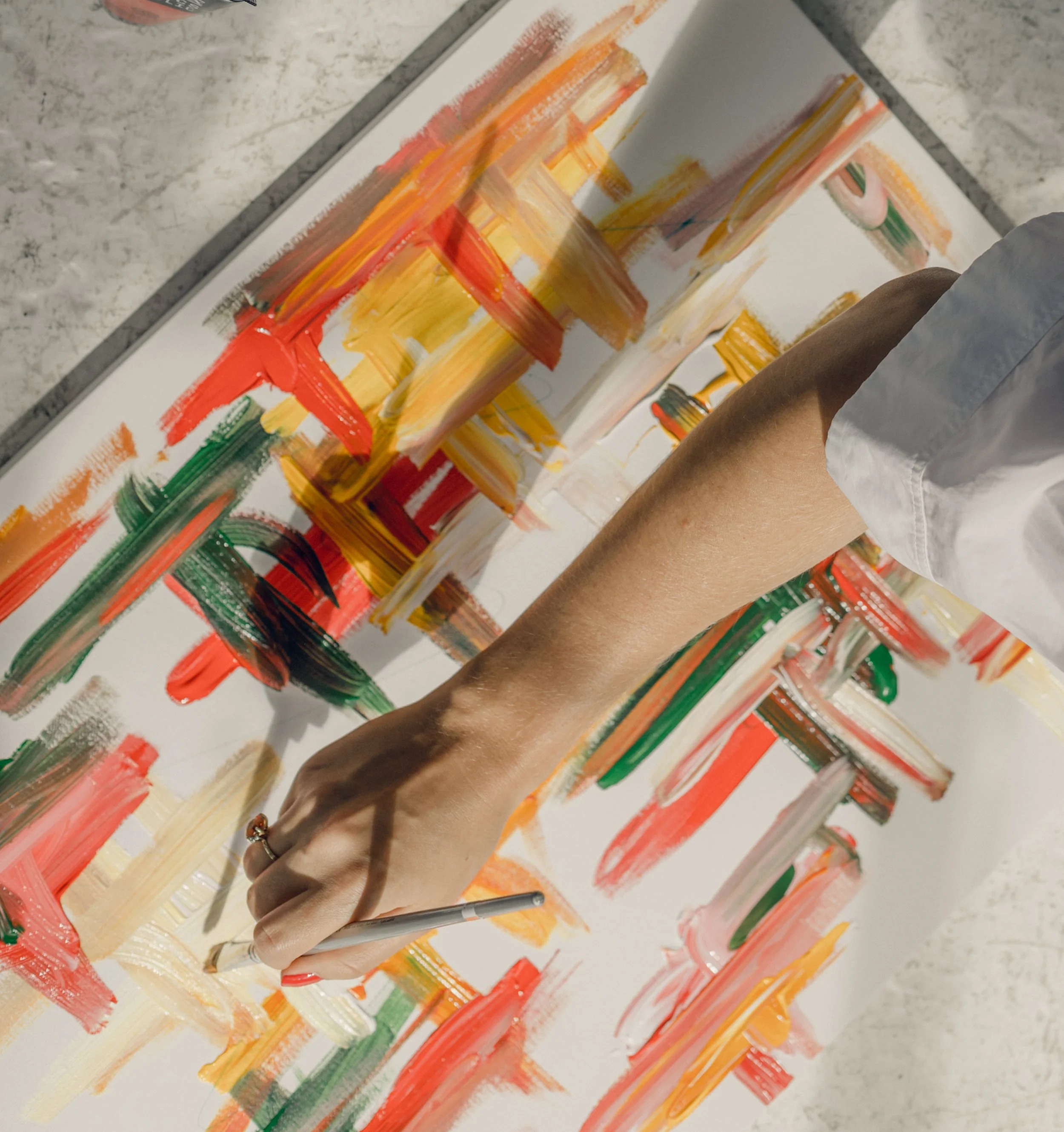 Kate's arm holding a paint brush over a brightly coloured canvas she's working on
