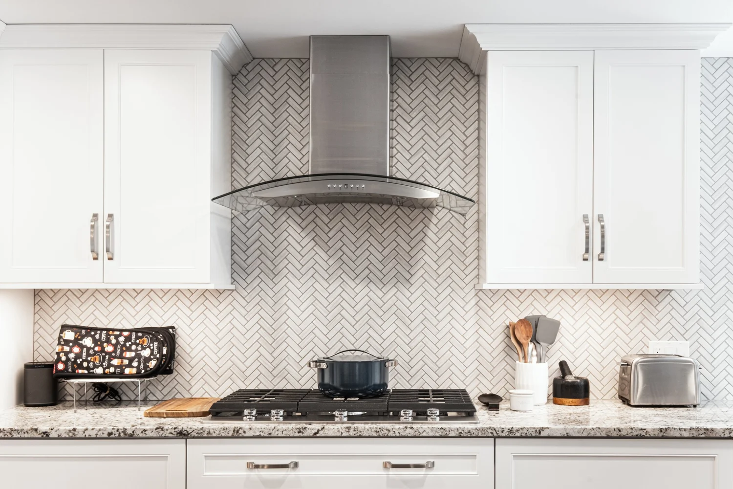 Stainless range hood over a herringbone backsplash and granite worktop