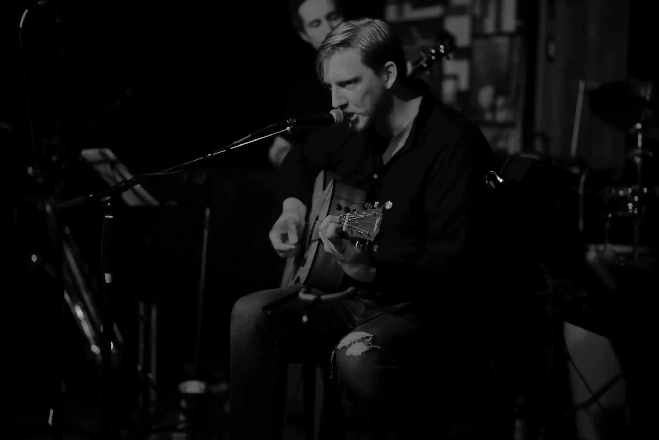 Black-and-white photograph of a Belleisle musician singing and playing acoustic guitar.