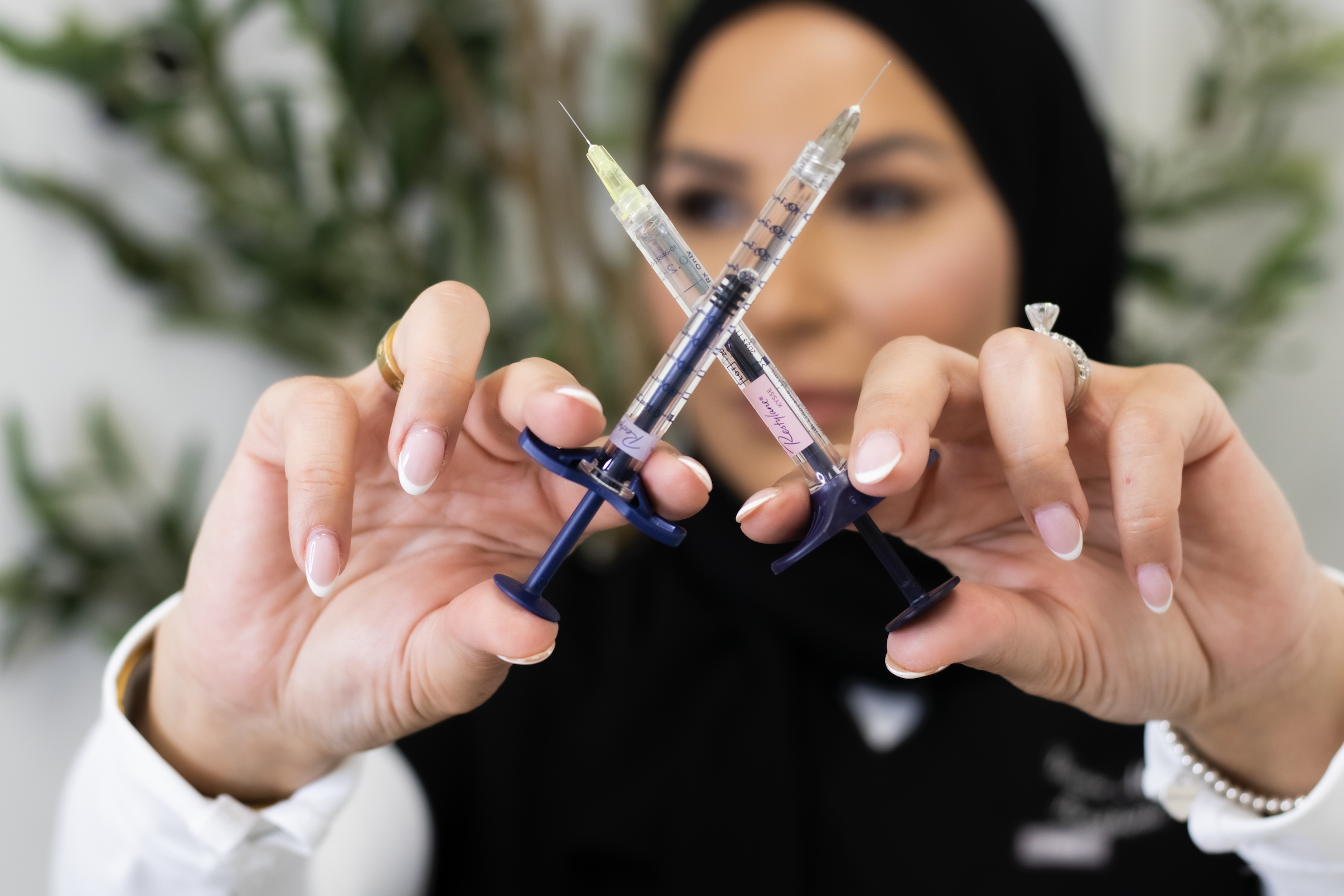 Een vrouw houdt drie injectiespuiten met naalden omhoog, terwijl ze in de camera kijkt.