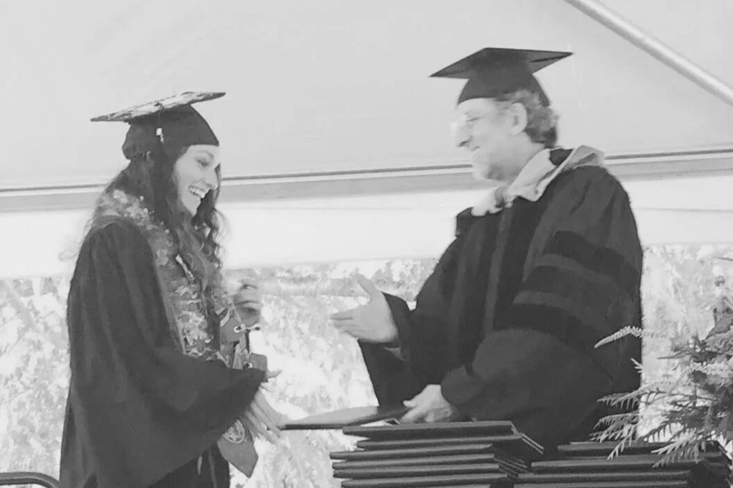 A black and white image of a young woman receiving a diploma.
