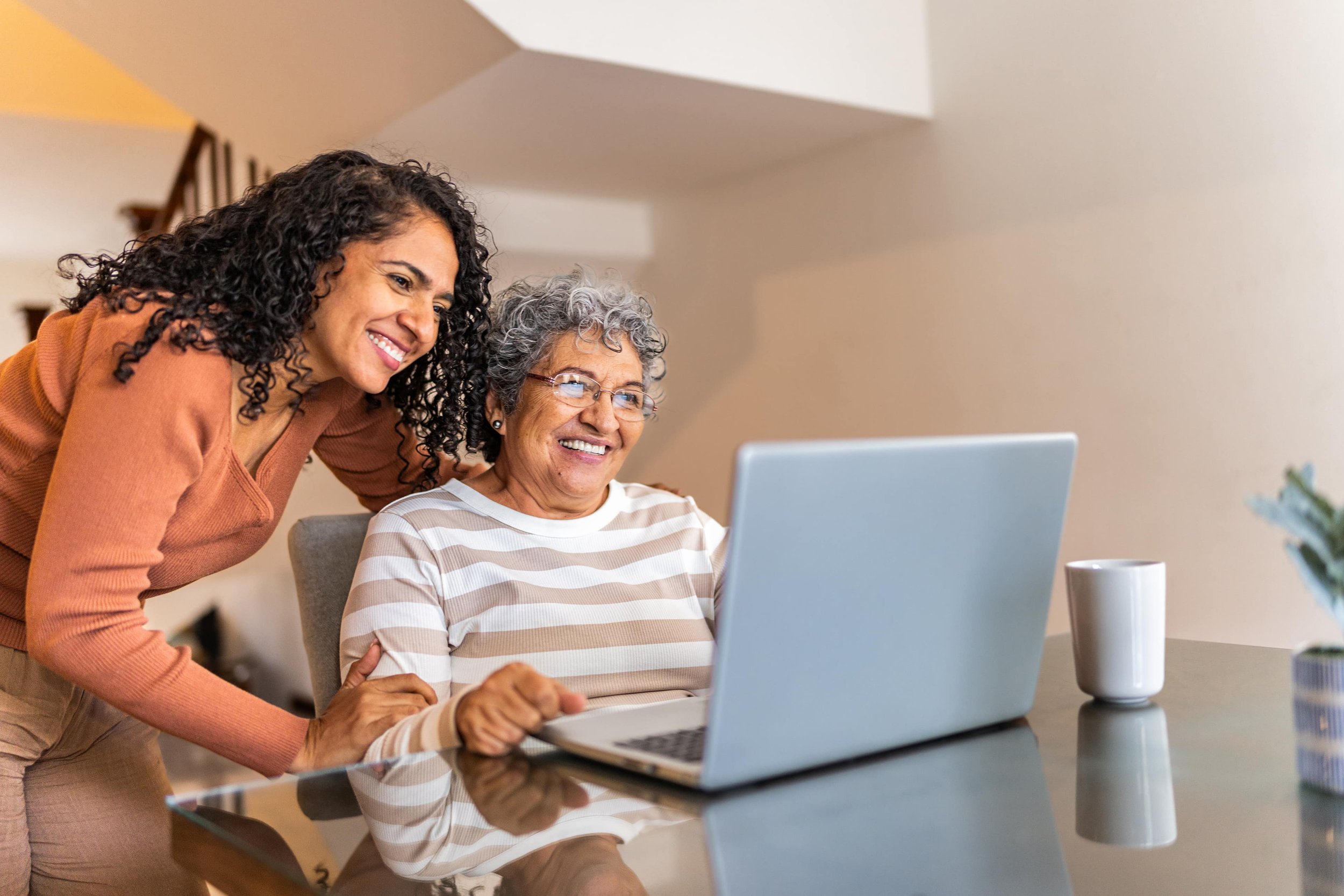 Two women, one younger and one older, looking at a laptop computer screen, smiling.