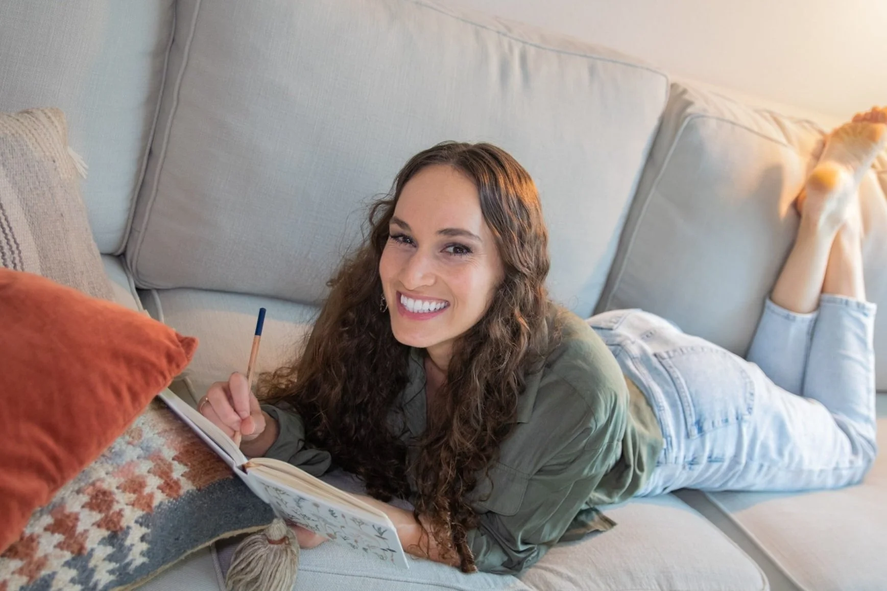 Web Designer for Therapists Maggie Goulder laying on a couch smiling and holding a notebook and a pencil.